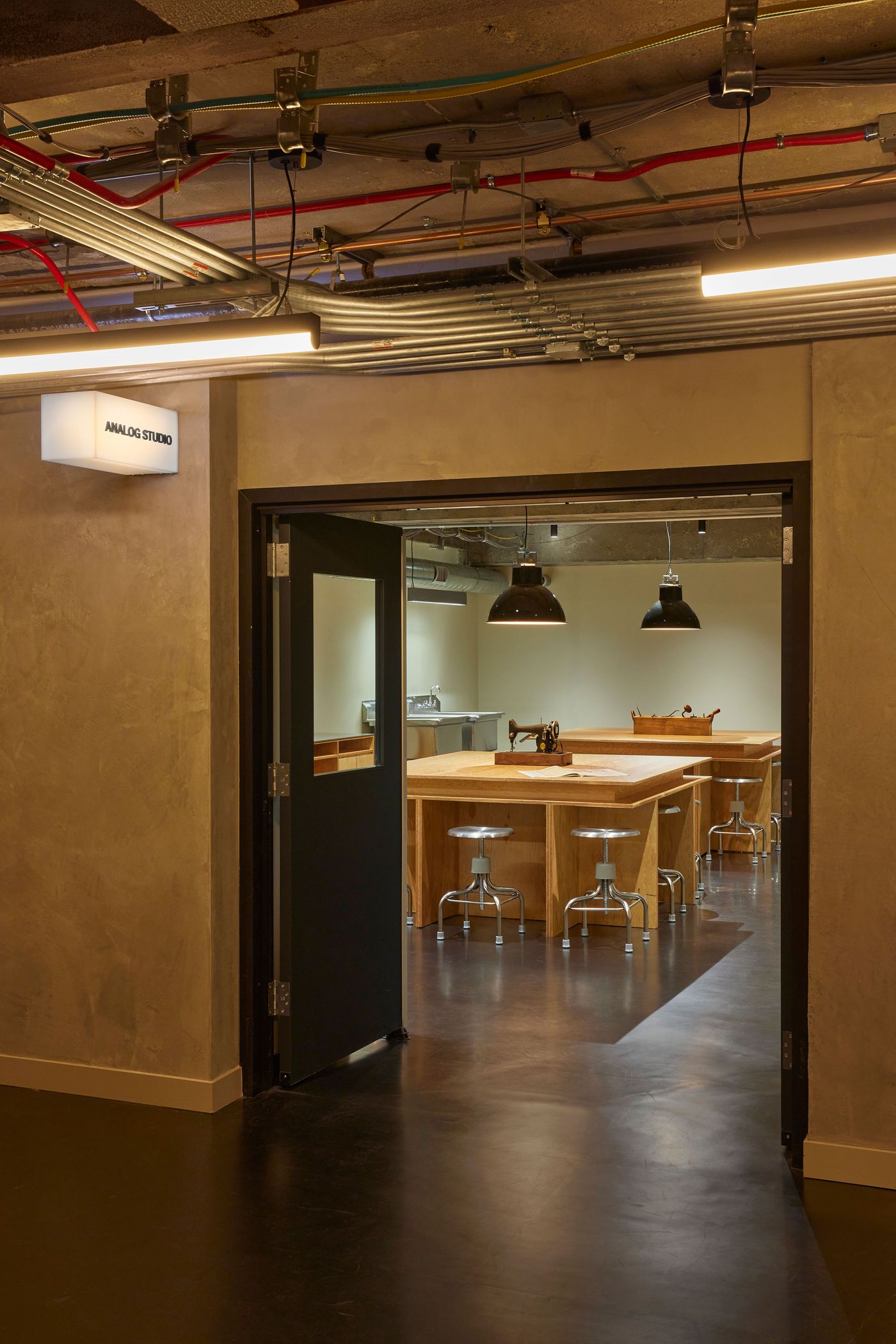 A doorway leads to a well-lit studio with wooden tables, metal stools, and industrial-style lighting, labeled "Analog Studio." A doorway leads to a well-lit studio with wooden tables, metal stools, and industrial-style lighting, labeled "Analog Studio."