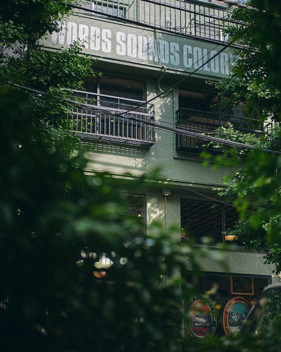 A building partially obscured by greenery, featuring the phrase "Words Sounds Colors" prominently displayed above its windows.