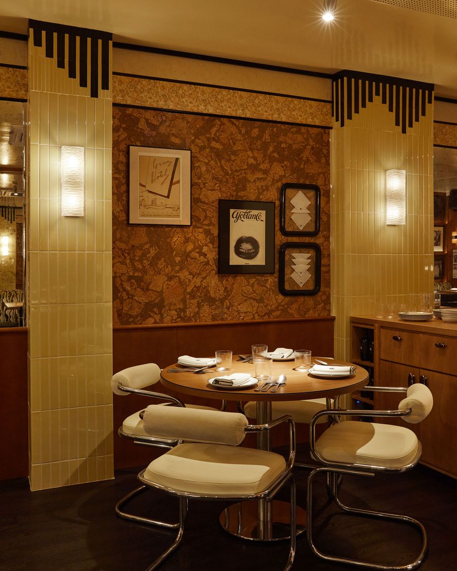 This image captures a cozy dining nook, blending Art Deco with mid-century modern design. The warm lighting highlights the glossy, yellow tiles and a decorative, wood-paneled wall. A small table is surrounded by sleek chrome-framed chairs, emphasizing a blend of graphic lines and soft, organic shapes. This image captures a cozy dining nook, blending Art Deco with mid-century modern design. The warm lighting highlights the glossy, yellow tiles and a decorative, wood-paneled wall. A small table is surrounded by sleek chrome-framed chairs, emphasizing a blend of graphic lines and soft, organic shapes.