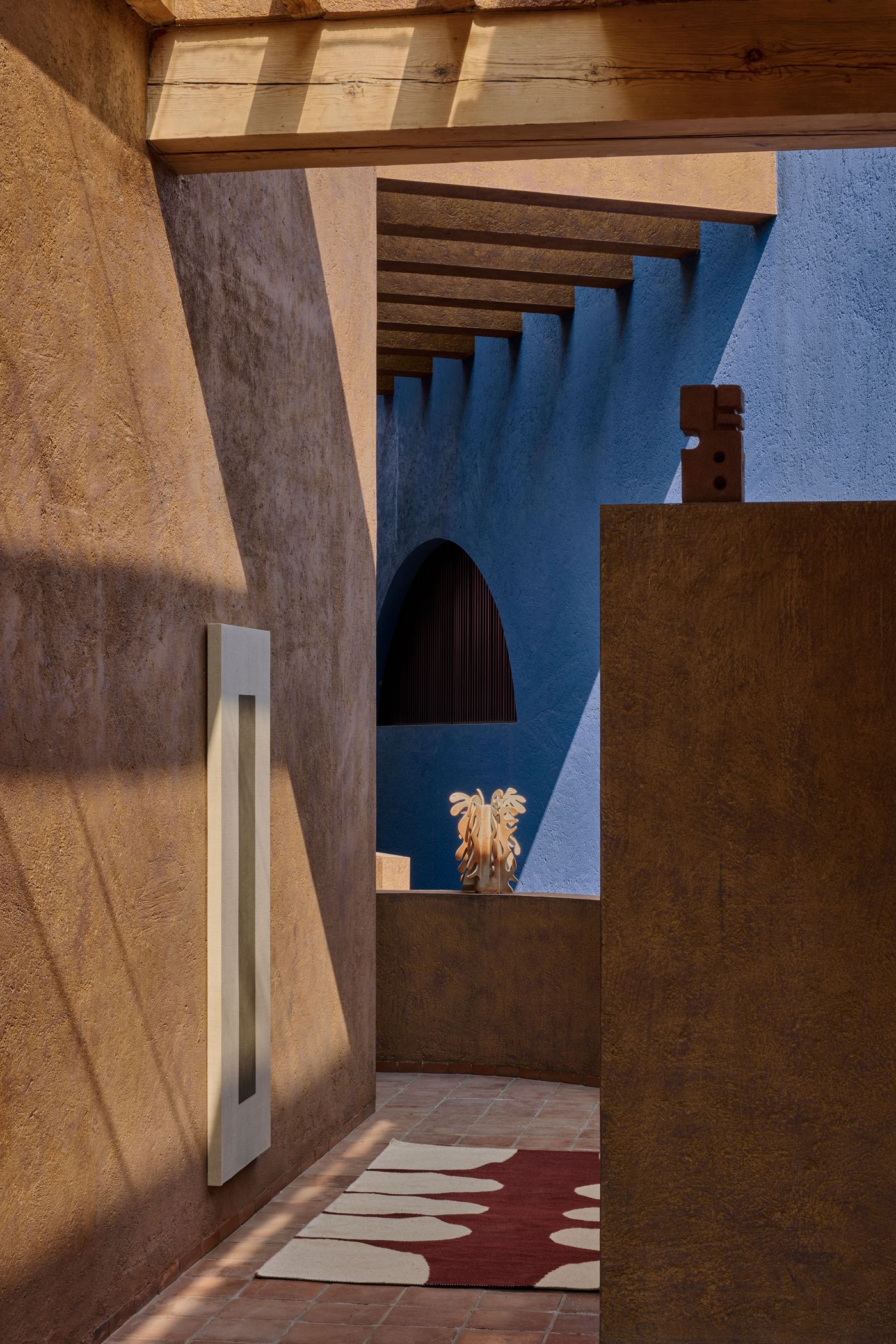 A colorful interior showcases textured brown and blue walls, wooden beams, and a decorative rug with a wooden sculpture in the foreground.