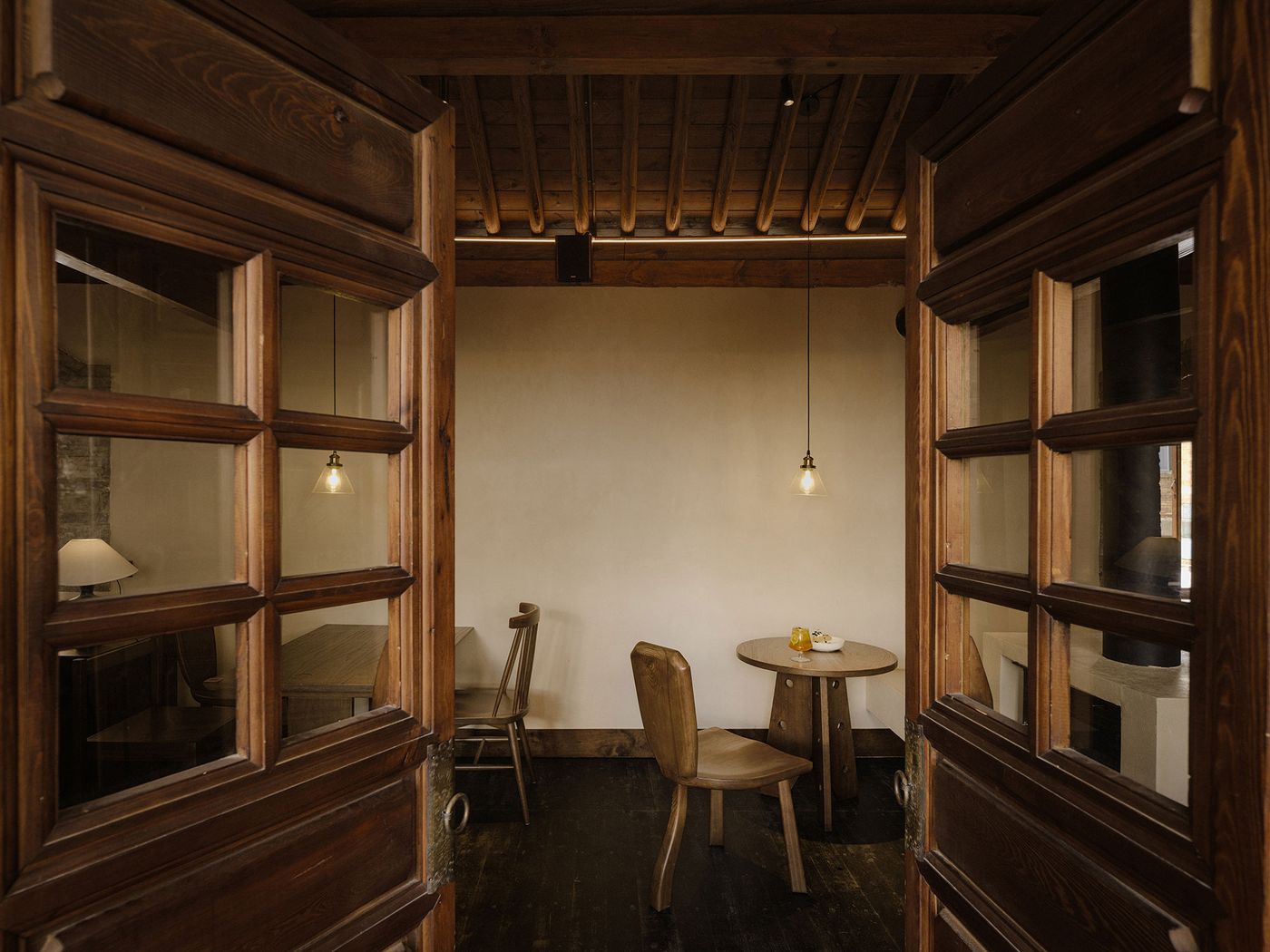 Two wooden doors open to a cozy, minimalist dining area with a round table, soft lighting, and a welcoming atmosphere. Two wooden doors open to a cozy, minimalist dining area with a round table, soft lighting, and a welcoming atmosphere.
