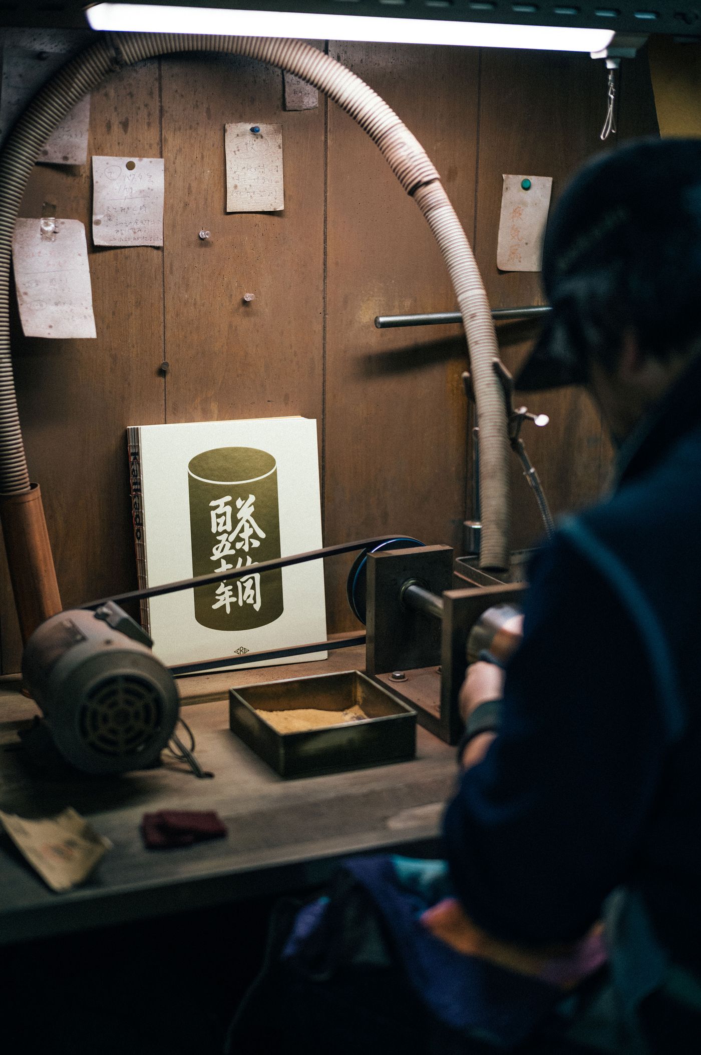 A craftsman works at a wooden desk, focusing on a book with Japanese characters, surrounded by tools and notes in a cozy workshop. A craftsman works at a wooden desk, focusing on a book with Japanese characters, surrounded by tools and notes in a cozy workshop.