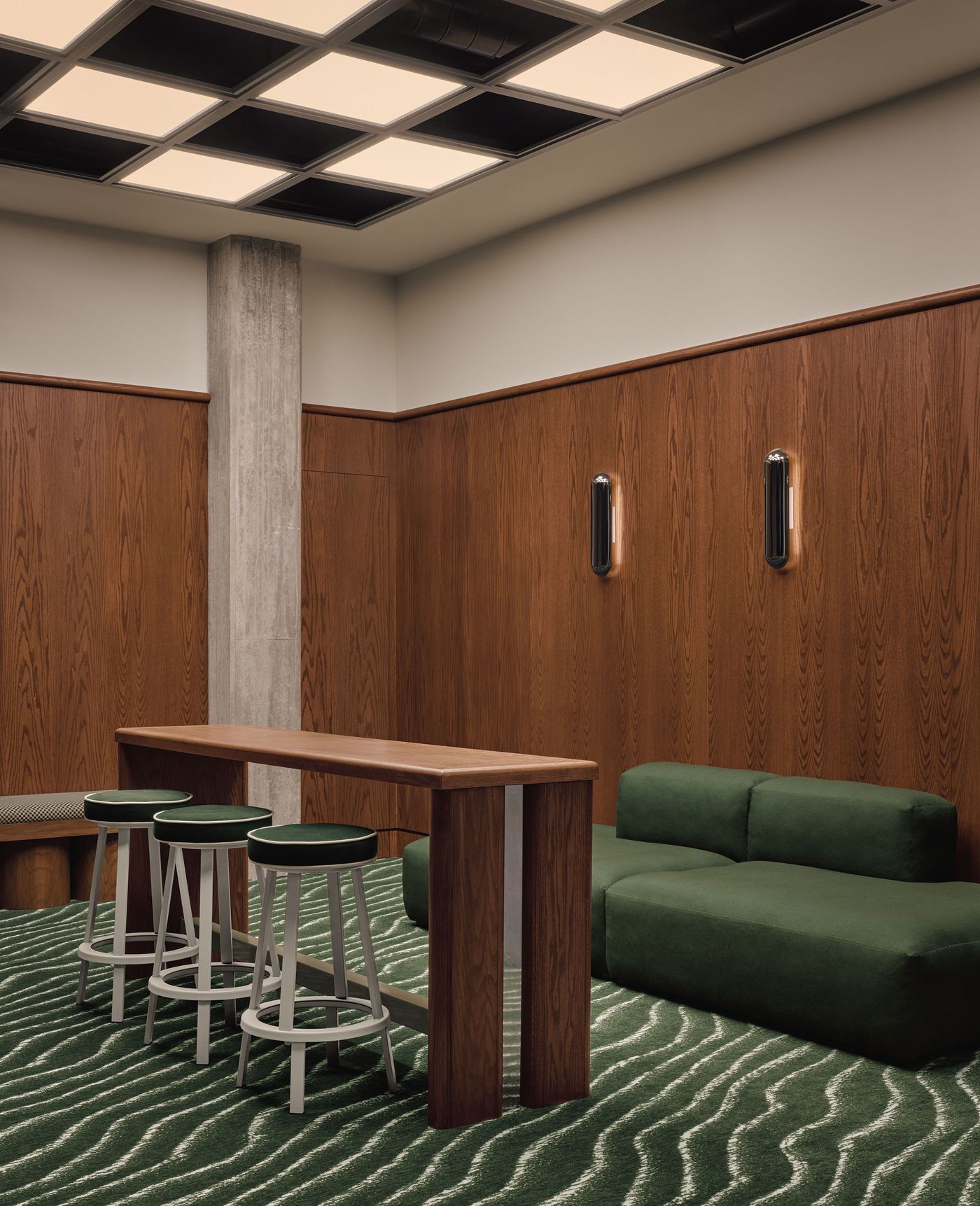 Stylish interior featuring a wooden wall, green carpet, and modern furniture: high table with stools and a plush green couch. Stylish interior featuring a wooden wall, green carpet, and modern furniture: high table with stools and a plush green couch.