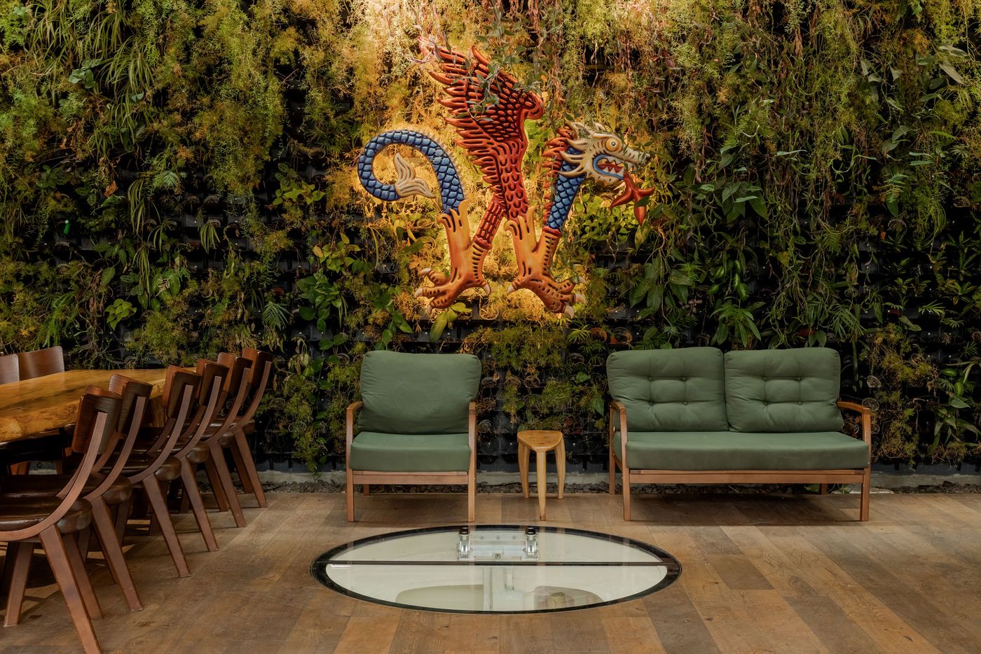 A cozy seating area with green sofas, a wooden table, and a vibrant dragon mural set against a lush vertical garden backdrop.
