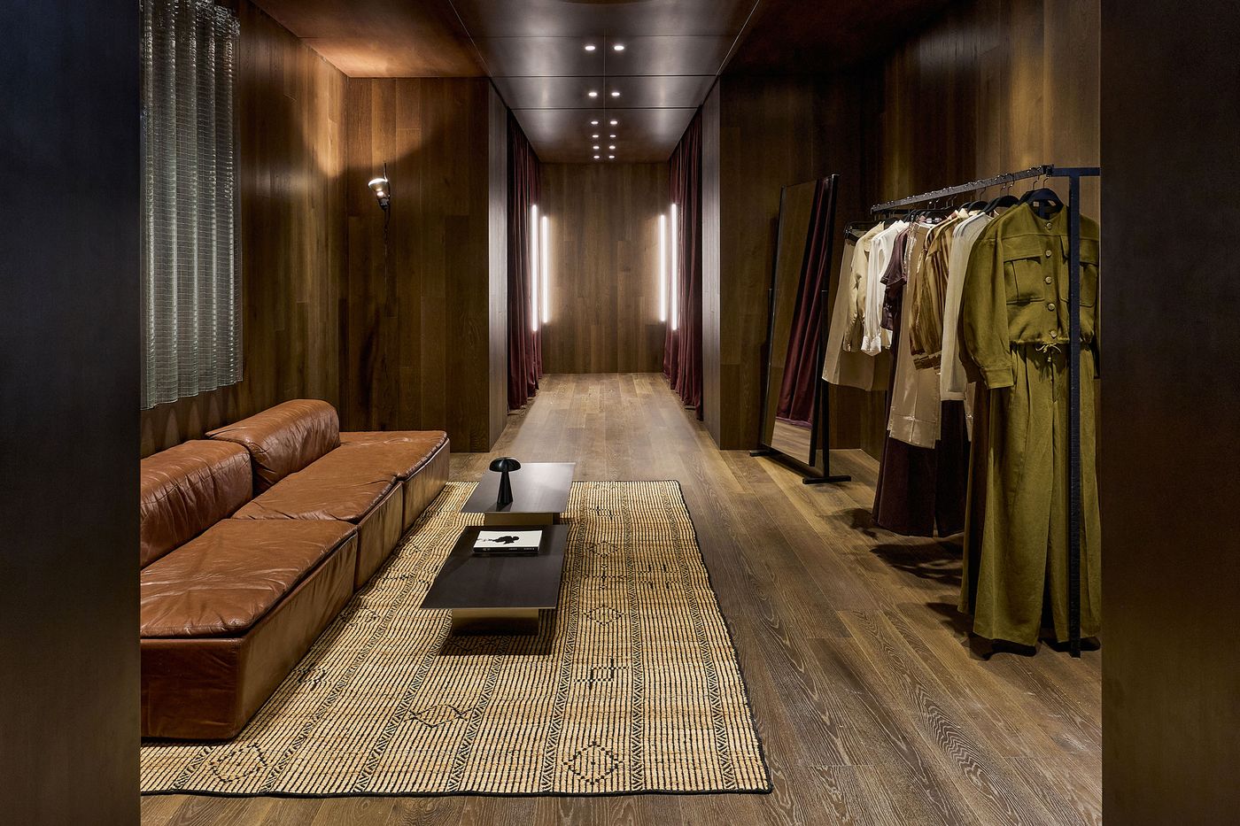 Stylish boutique interior featuring a brown leather sofa, a modern coffee table, and a rack of elegant clothing against wooden walls.