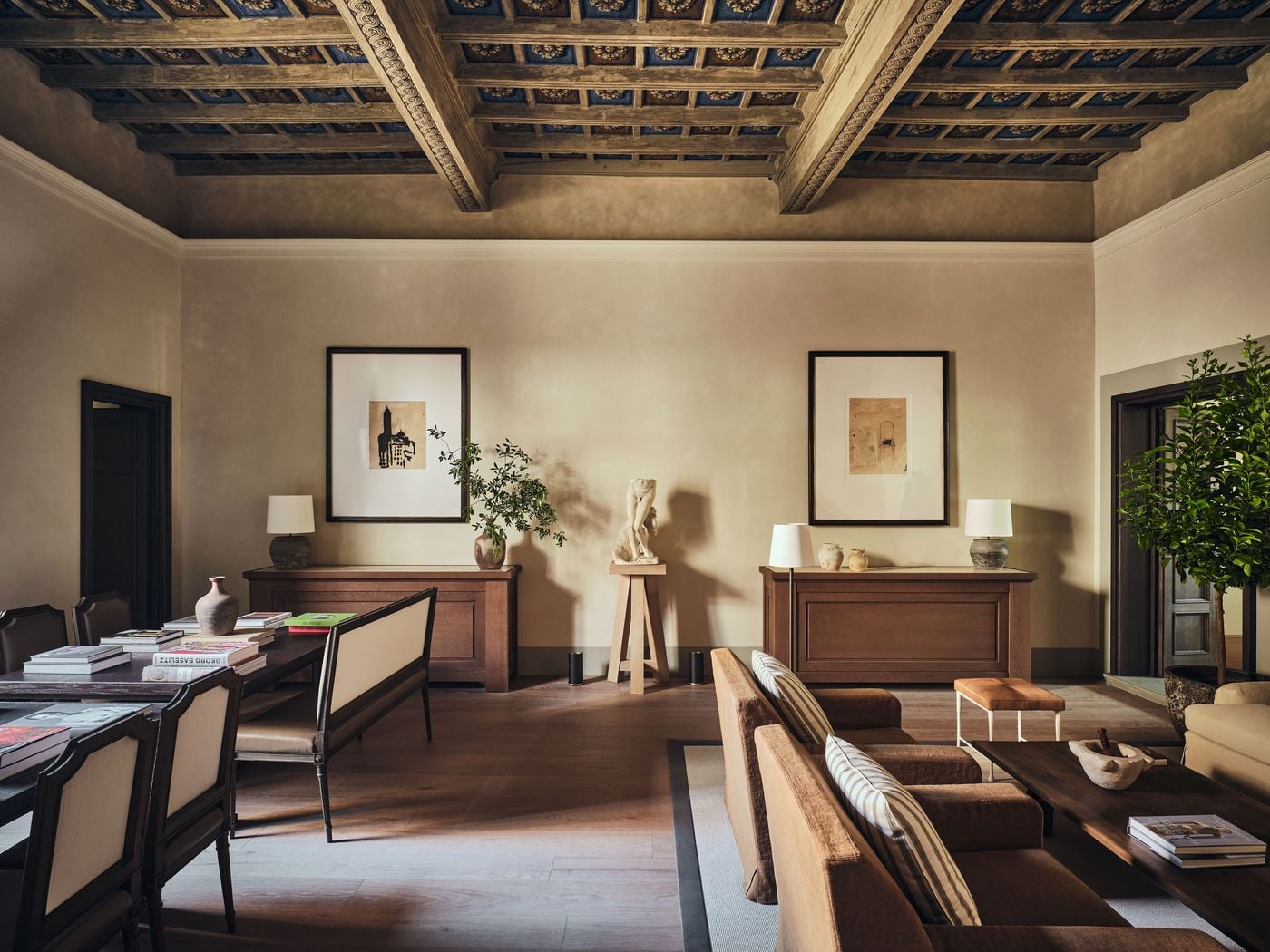 A carved and painted coffered ceiling in deep blue and gold crowns a shared living space at La Réserve Firenze. Below, a headless classical torso on a timber stand sits between oak sideboards and framed works on paper, while art books on a long table and a potted citrus tree lend the room a lived-in ease. A carved and painted coffered ceiling in deep blue and gold crowns a shared living space at La Réserve Firenze. Below, a headless classical torso on a timber stand sits between oak sideboards and framed works on paper, while art books on a long table and a potted citrus tree lend the room a lived-in ease.