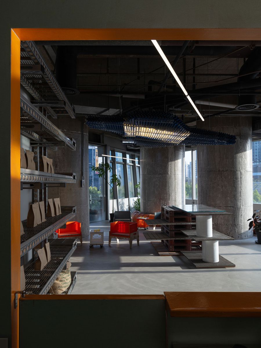 A captivating view into a lounge area within 889 GLO Art Space, featuring vibrant orange chairs that add a pop of color against the raw concrete. A unique, sculptural light fixture hangs from the exposed ceiling, while a glass-topped table constructed from stacked wooden pallets and a white column exemplifies creative reuse and industrial-meets-artistic design. A captivating view into a lounge area within 889 GLO Art Space, featuring vibrant orange chairs that add a pop of color against the raw concrete. A unique, sculptural light fixture hangs from the exposed ceiling, while a glass-topped table constructed from stacked wooden pallets and a white column exemplifies creative reuse and industrial-meets-artistic design.