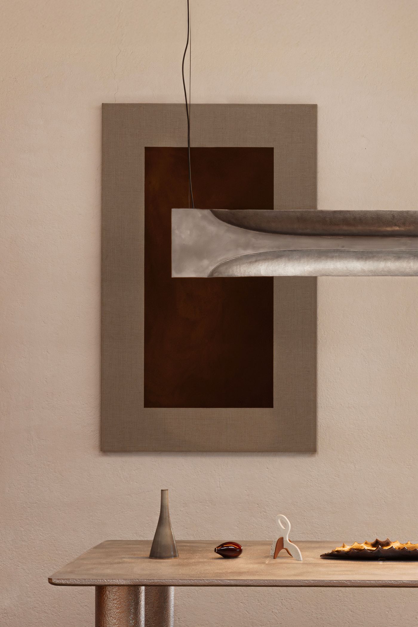 A modern art display featuring a metal light fixture, a textured wall panel, and minimalist decor on a stylish table.