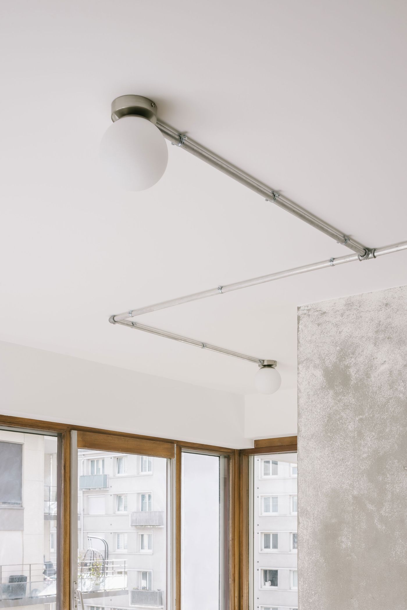 Modern ceiling lighting with spherical white bulbs and industrial metal piping, illuminating a minimalist room with large windows.