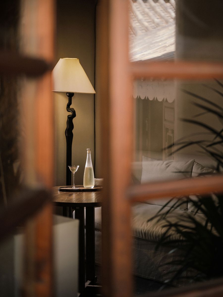 A cozy interior view featuring a stylish lamp, a table with a cocktail glass and a bottle, and a soft sofa in a warm atmosphere. A cozy interior view featuring a stylish lamp, a table with a cocktail glass and a bottle, and a soft sofa in a warm atmosphere.