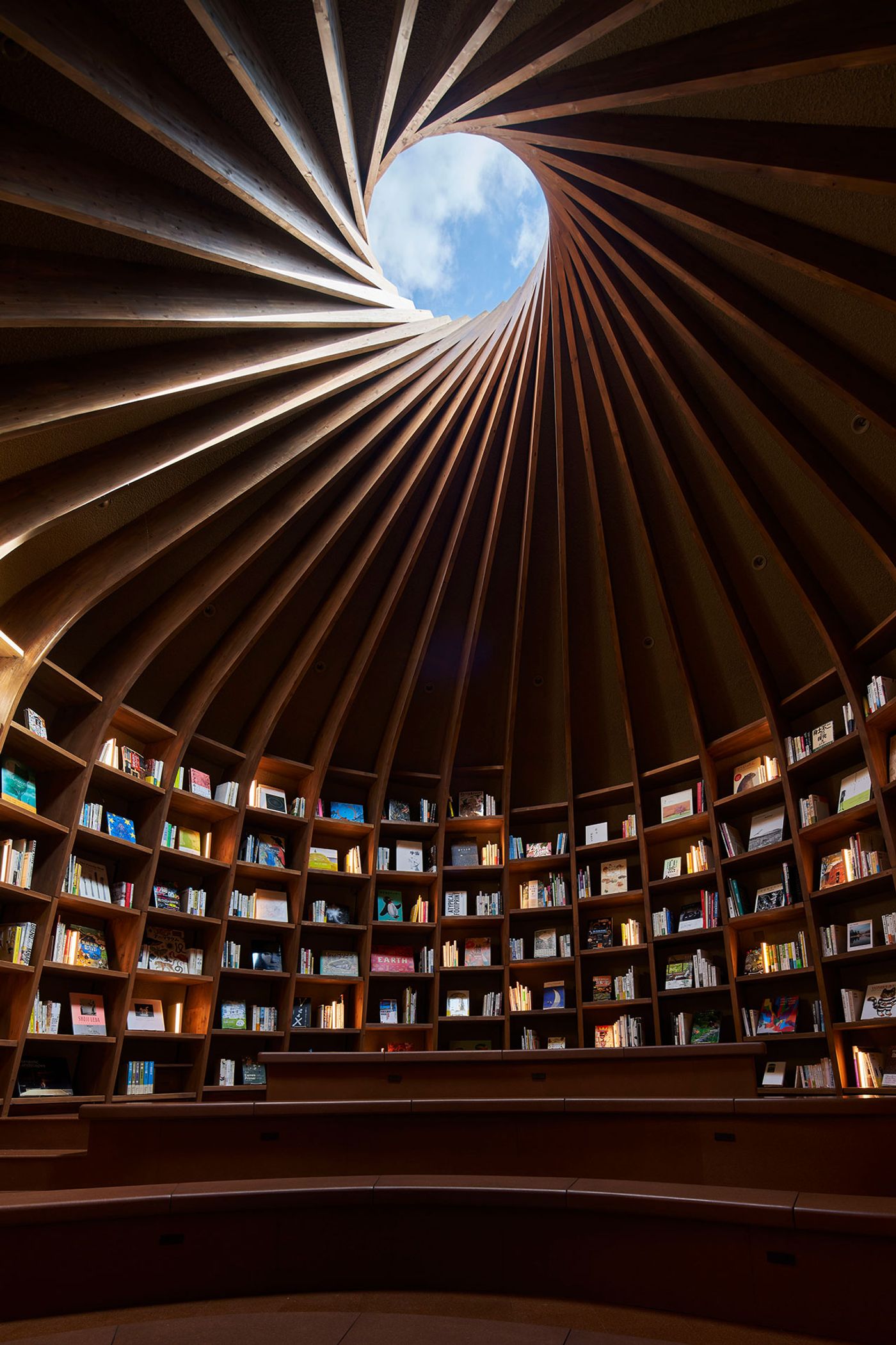 A spiraled wooden library interior with shelves filled with books, featuring a circular skylight that illuminates the space. A spiraled wooden library interior with shelves filled with books, featuring a circular skylight that illuminates the space.