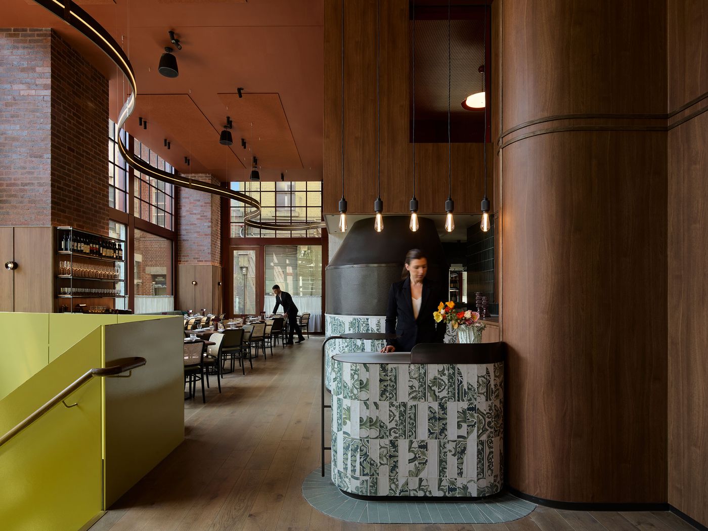 A modern restaurant interior featuring wooden walls, stylish seating, and a vibrant green staircase, with a flower-adorned reception desk. A modern restaurant interior featuring wooden walls, stylish seating, and a vibrant green staircase, with a flower-adorned reception desk.