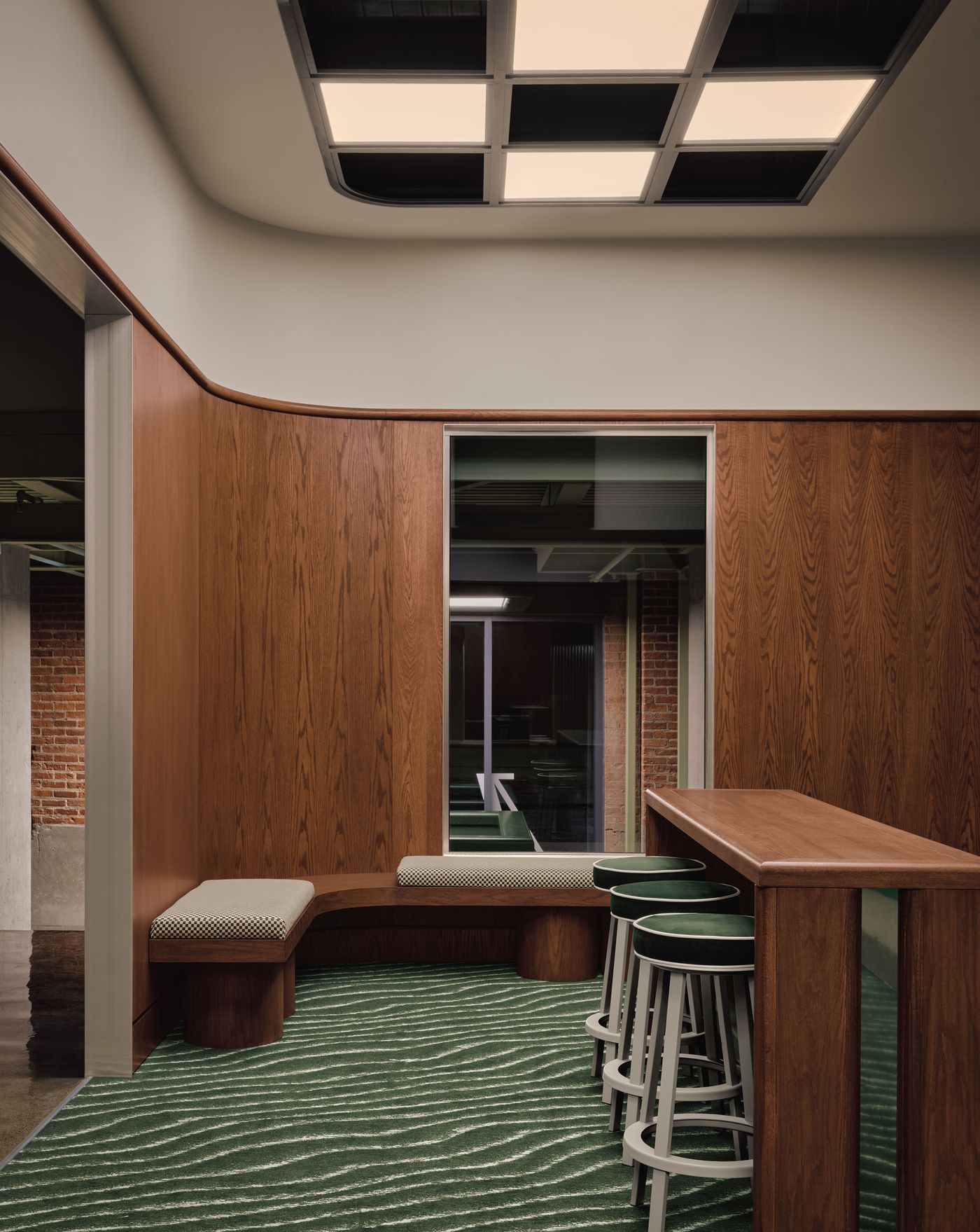 Modern interior featuring curved wooden walls, a cozy seating area, a bar with green stools, and textured green carpet. Modern interior featuring curved wooden walls, a cozy seating area, a bar with green stools, and textured green carpet.