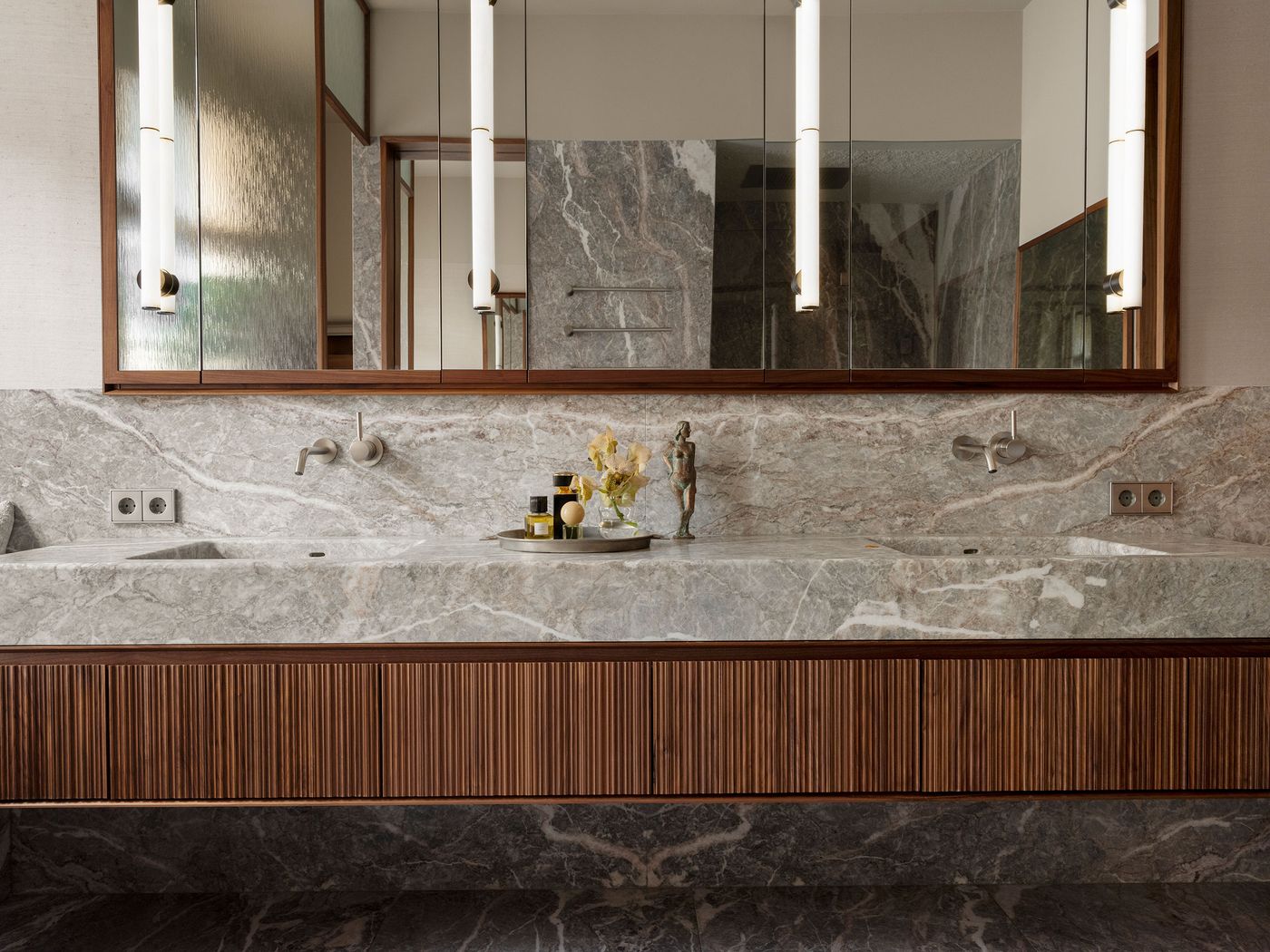 Modern bathroom with a sleek gray marble vanity, wooden cabinetry, stylish lighting, and decorative accents including flowers and a sculpture. Modern bathroom with a sleek gray marble vanity, wooden cabinetry, stylish lighting, and decorative accents including flowers and a sculpture.
