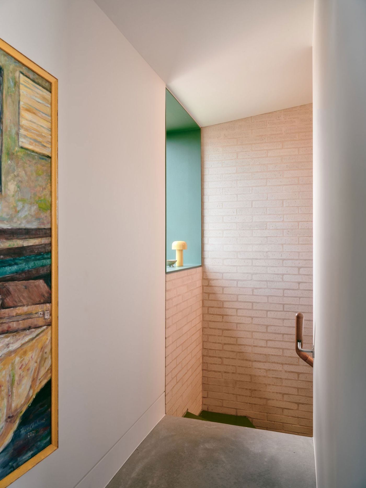 The stairwell combines pale exposed brick with crisp white walls and a deep sage-green recess, continuing Denj Lane’s material and colour palette indoors. A small yellow lamp glows within the niche, while an expressive painting and timber handrail bring warmth and domestic character to the restrained transitional space. The stairwell combines pale exposed brick with crisp white walls and a deep sage-green recess, continuing Denj Lane’s material and colour palette indoors. A small yellow lamp glows within the niche, while an expressive painting and timber handrail bring warmth and domestic character to the restrained transitional space.