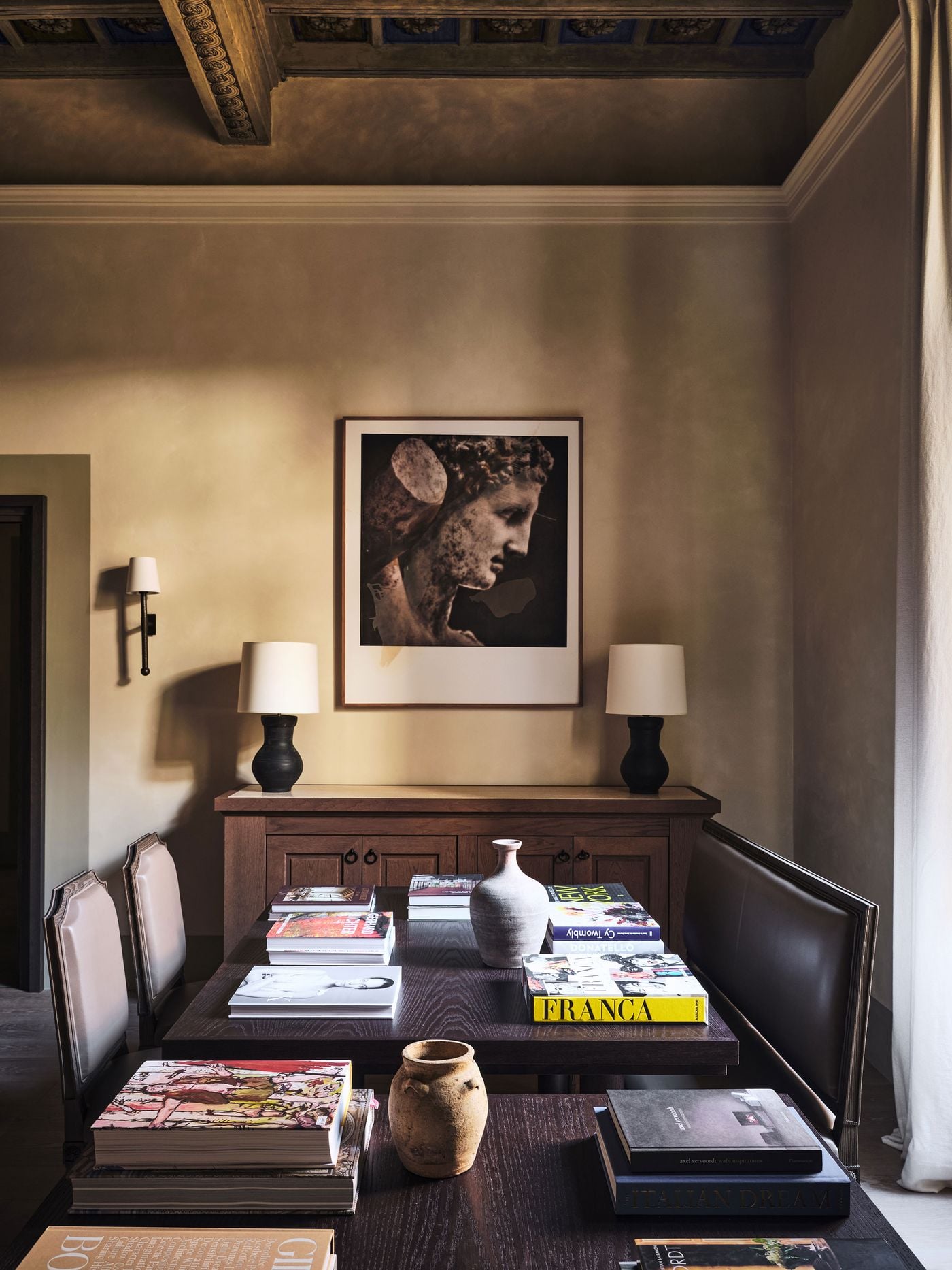 A large photographic print of a classical marble head in profile hangs above an oak sideboard flanked by black ceramic lamps at La Réserve Firenze. In the foreground, tables stacked with monographs on Cy Twombly, Donatello and Gerhard Richter sit beside earthenware vessels and a leather-backed bench. A large photographic print of a classical marble head in profile hangs above an oak sideboard flanked by black ceramic lamps at La Réserve Firenze. In the foreground, tables stacked with monographs on Cy Twombly, Donatello and Gerhard Richter sit beside earthenware vessels and a leather-backed bench.