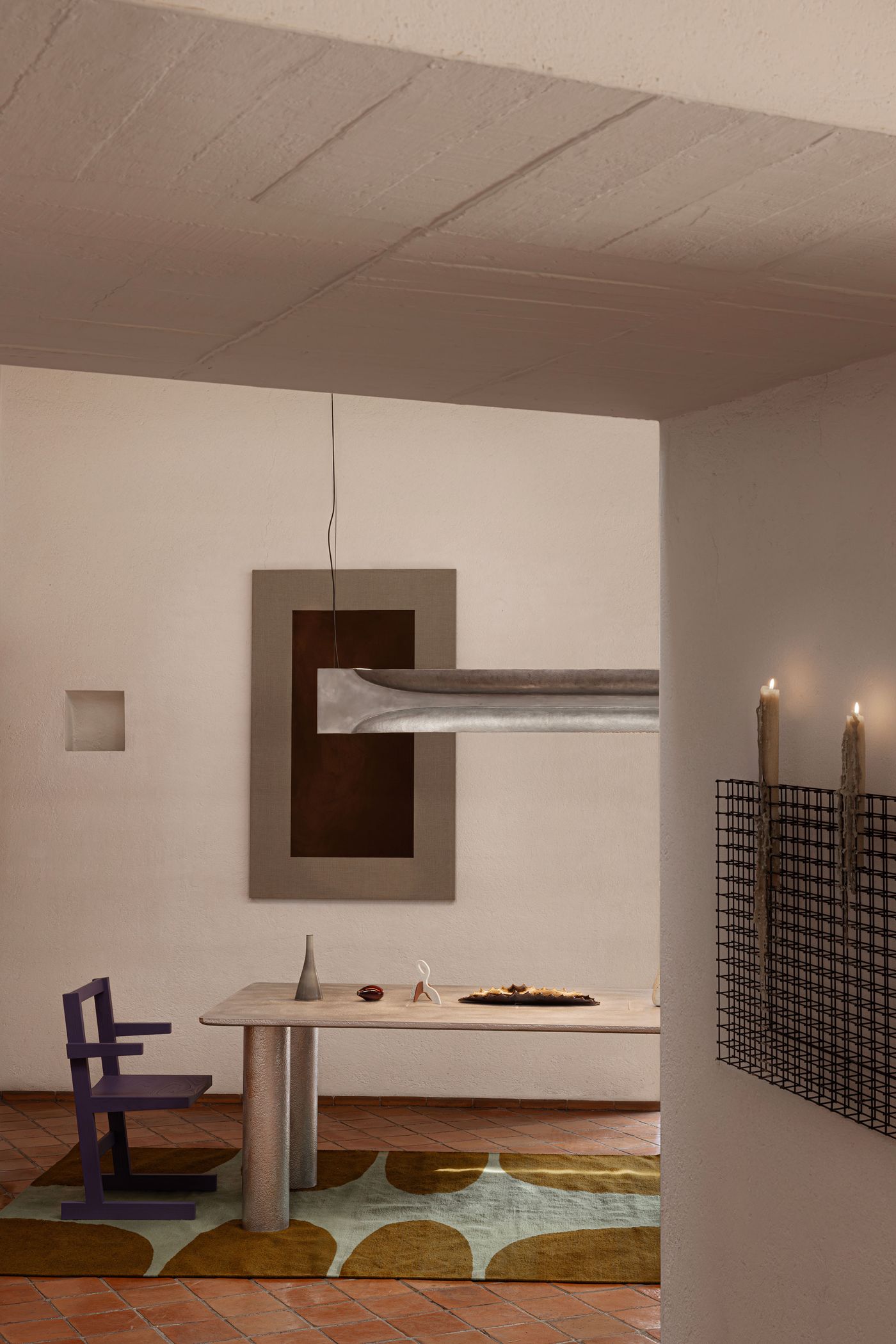 A modern dining area featuring a concrete table, colorful rug, purple chair, and minimalist decor on the walls.