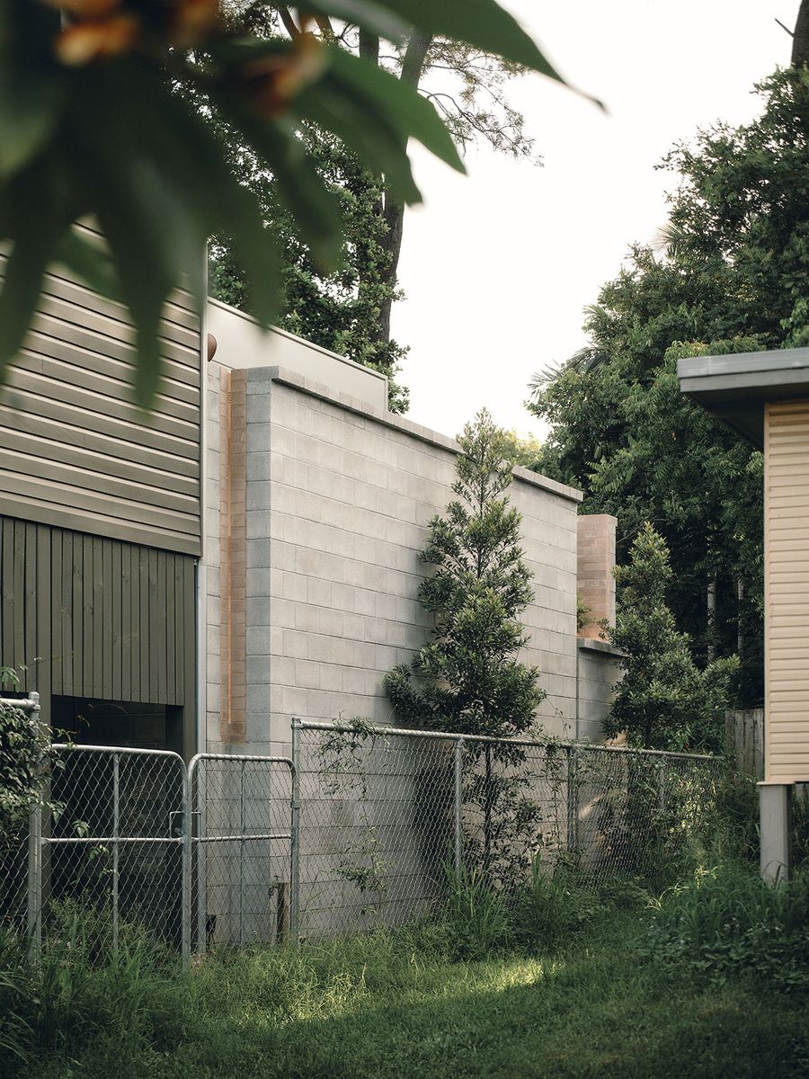 A view of two modern buildings separated by a chain-link fence, surrounded by lush greenery and trees in a quiet backyard setting. A view of two modern buildings separated by a chain-link fence, surrounded by lush greenery and trees in a quiet backyard setting.