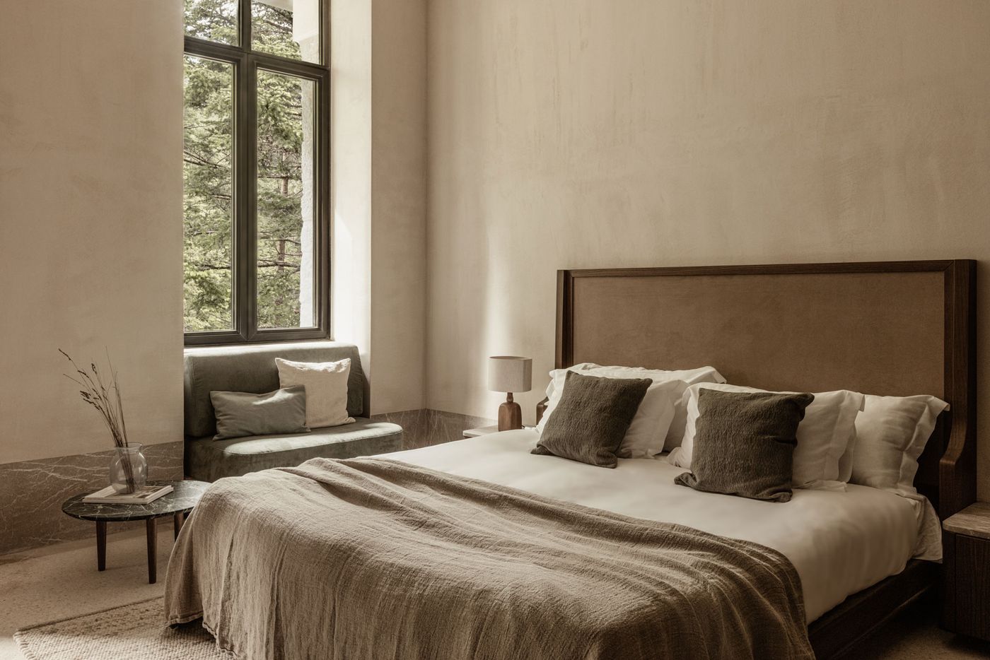 A tranquil bedroom with a focus on natural materials and a muted color palette. A large, dark-framed window overlooks a forest, while a cozy window seat invites relaxation. The bed features a minimalist wooden headboard, soft linen bedding in earthy tones, and two olive-green pillows, creating a serene and grounded atmosphere. A tranquil bedroom with a focus on natural materials and a muted color palette. A large, dark-framed window overlooks a forest, while a cozy window seat invites relaxation. The bed features a minimalist wooden headboard, soft linen bedding in earthy tones, and two olive-green pillows, creating a serene and grounded atmosphere.