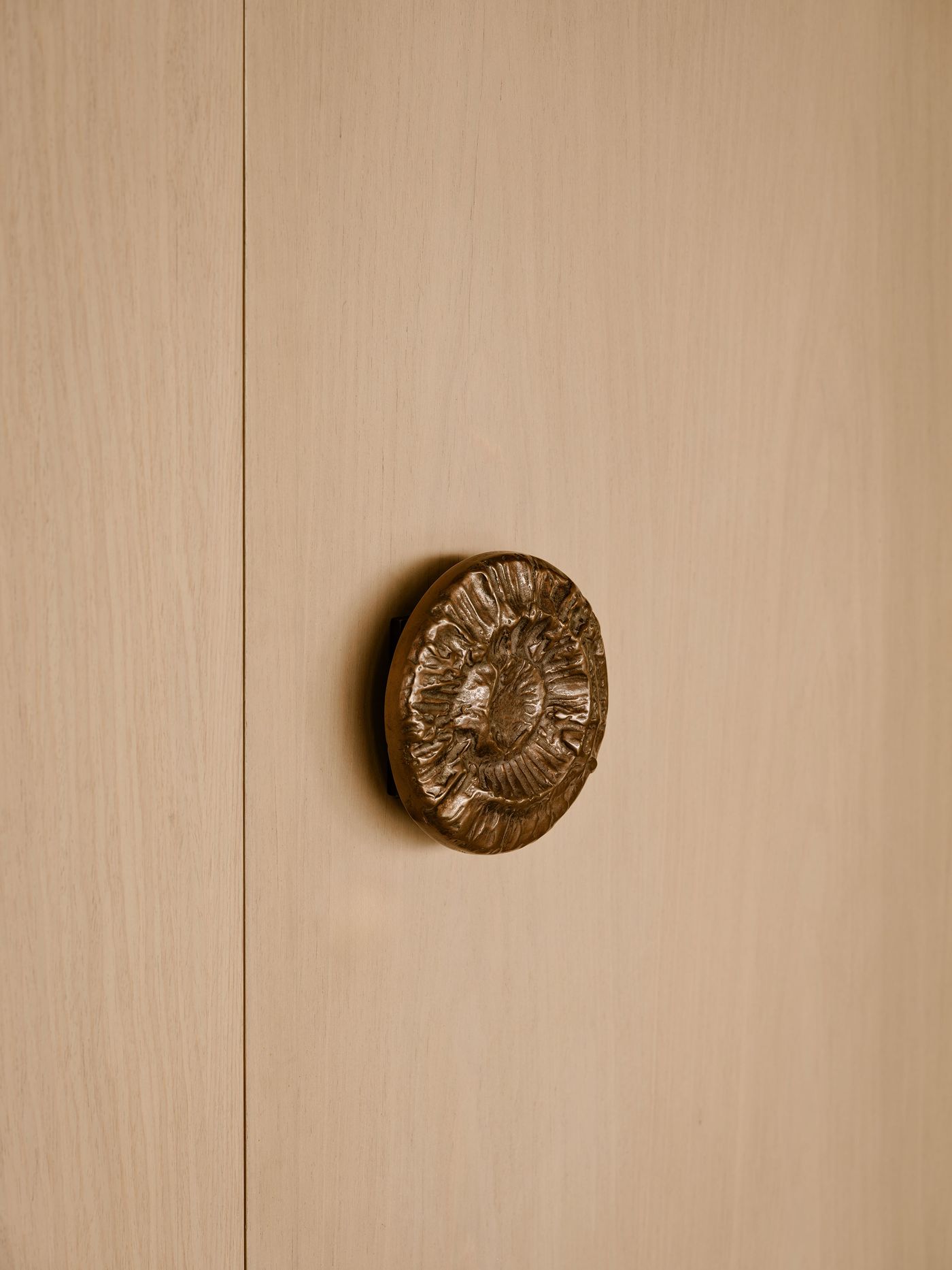 Close-up of a decorative bronze door knob on a light wooden door, featuring intricate floral patterns and smooth wood texture.