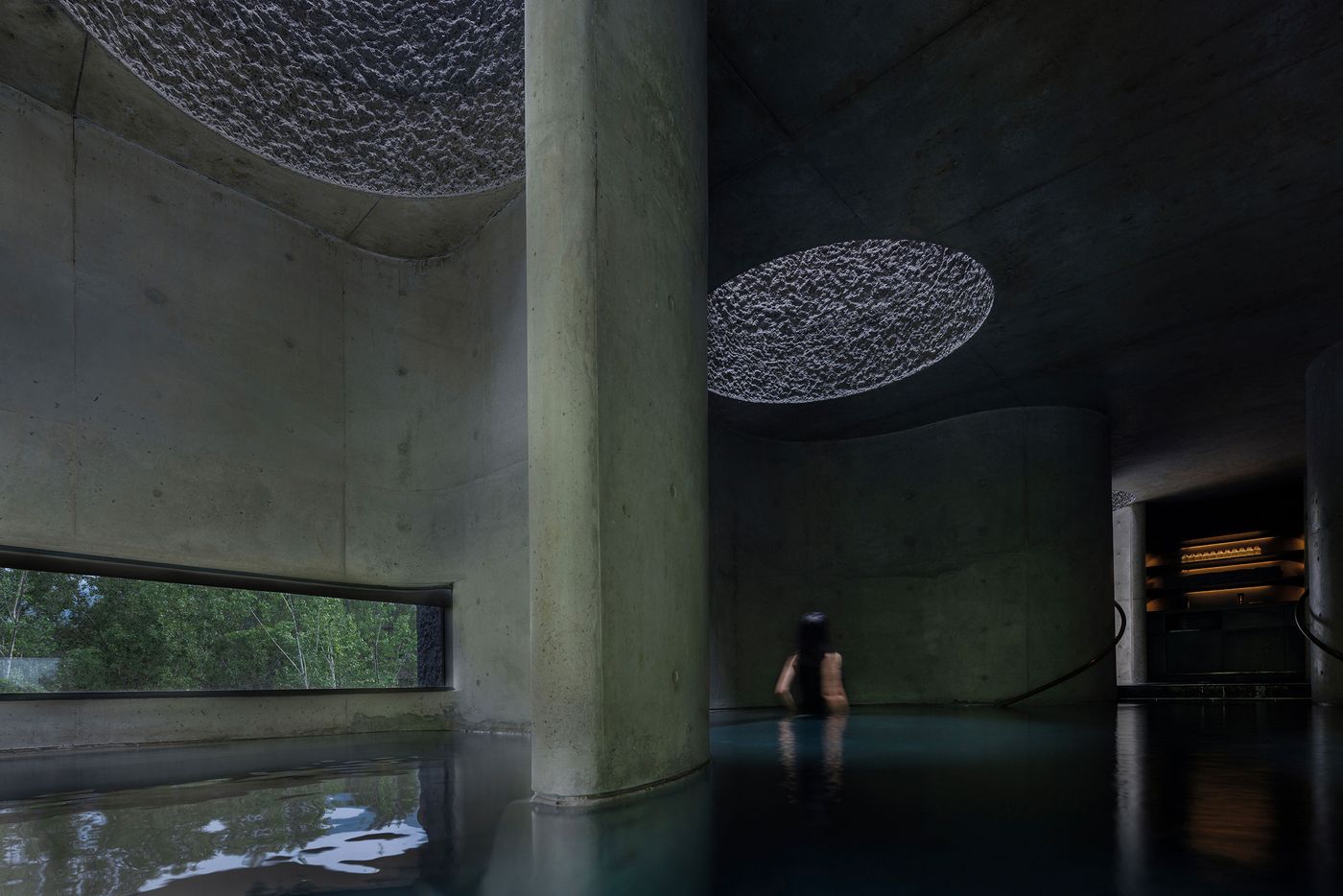 A serene, dimly lit interior with smooth concrete walls, featuring a person in a reflective pool beneath textured skylights. A serene, dimly lit interior with smooth concrete walls, featuring a person in a reflective pool beneath textured skylights.