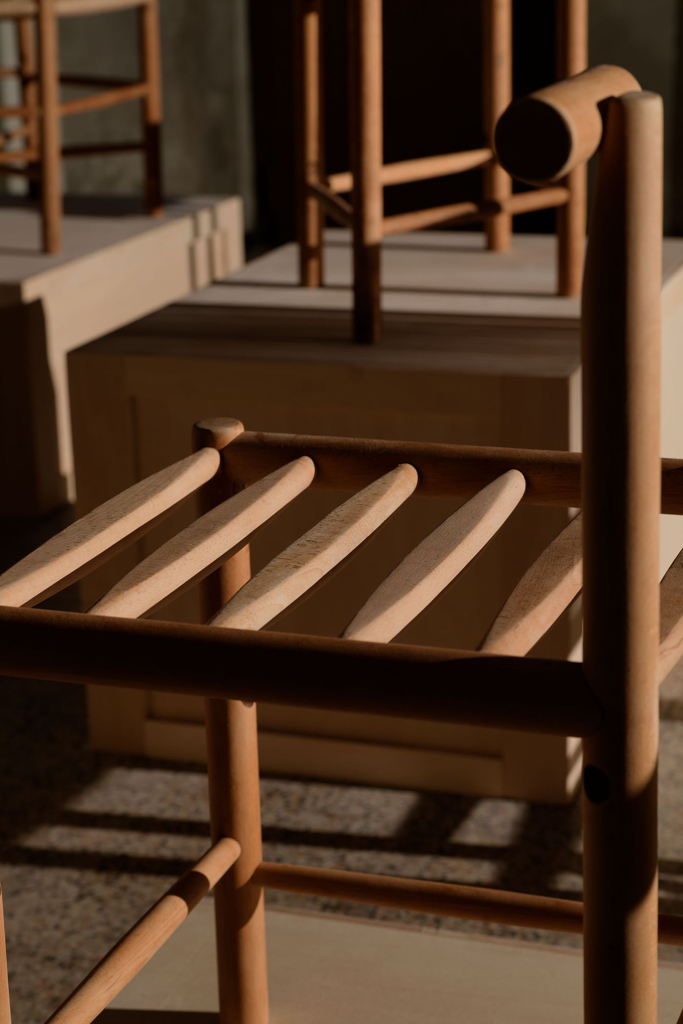 Close-up of a wooden chair, showcasing its slatted seat and smooth finish, with soft shadows and warm lighting in a serene setting.