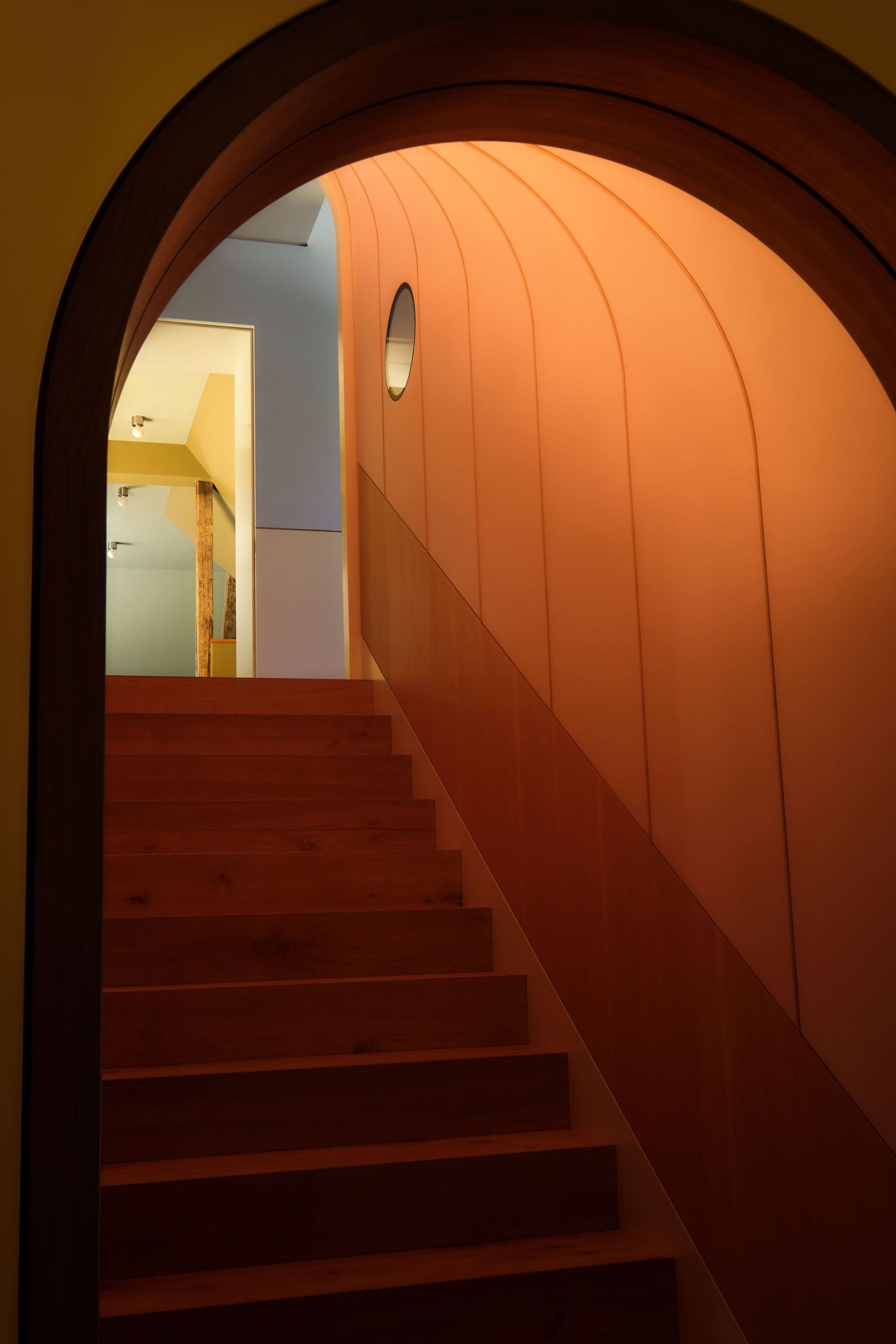 A cozy stairway with wooden steps leads through a warm, curved archway featuring orange and yellow tones, accented by soft lighting.