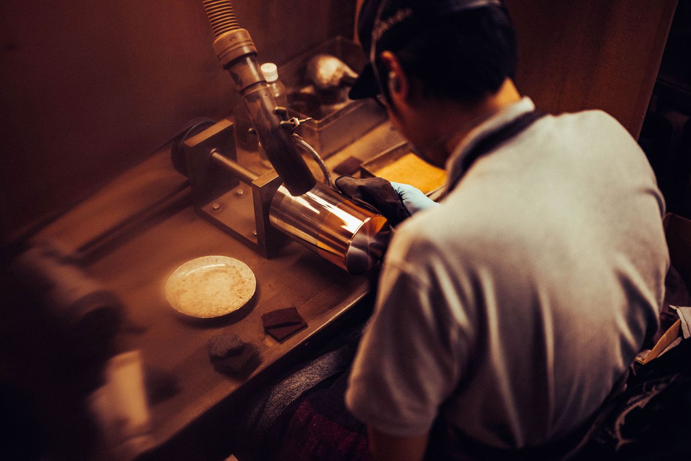 A craftsman carefully polishes a metallic object in a workshop, surrounded by tools and materials, focused on achieving a smooth finish. A craftsman carefully polishes a metallic object in a workshop, surrounded by tools and materials, focused on achieving a smooth finish.