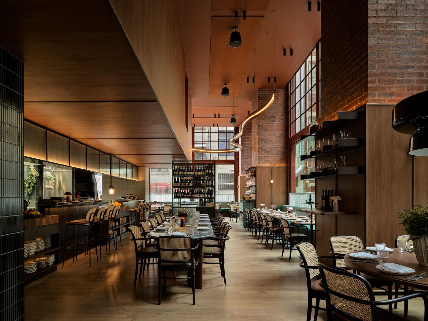 Modern restaurant interior featuring wooden decor, large windows, and stylish seating arrangements. Warm lighting enhances the ambiance.