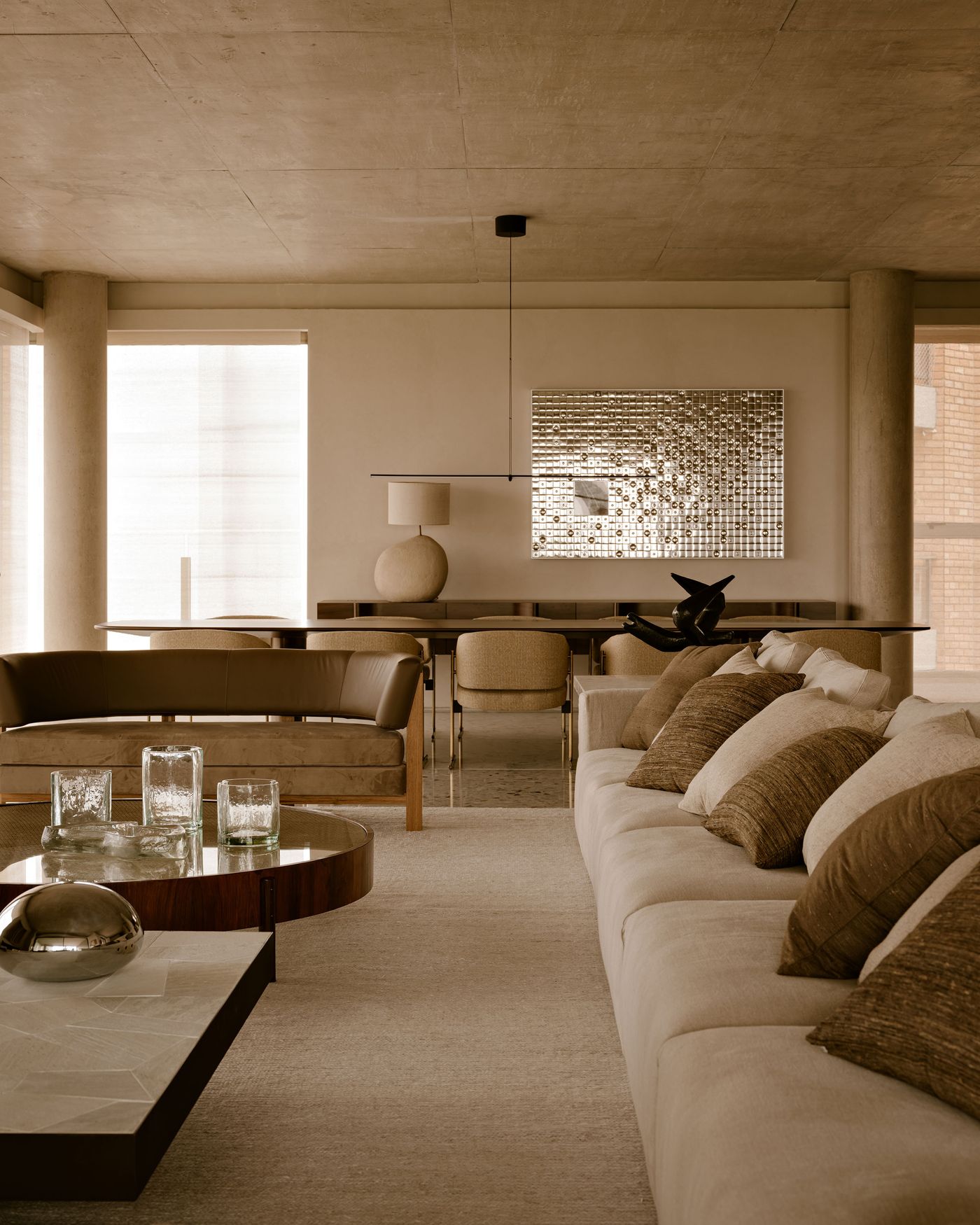 Modern living room featuring a plush sofa with textured pillows, minimalist decor, a glass table, and warm, muted tones. Modern living room featuring a plush sofa with textured pillows, minimalist decor, a glass table, and warm, muted tones.