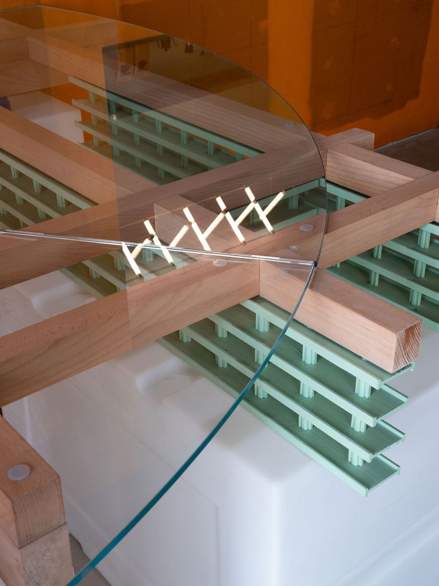 A close-up detail of a glass-topped table in 889 GLO Art Space, revealing the thoughtful design of its wooden beam structure and the subtle, pale green grating underneath. The reflection of light on the glass surface and the precise joinery reflect a commitment to both industrial honesty and minimalist craftsmanship. A close-up detail of a glass-topped table in 889 GLO Art Space, revealing the thoughtful design of its wooden beam structure and the subtle, pale green grating underneath. The reflection of light on the glass surface and the precise joinery reflect a commitment to both industrial honesty and minimalist craftsmanship.