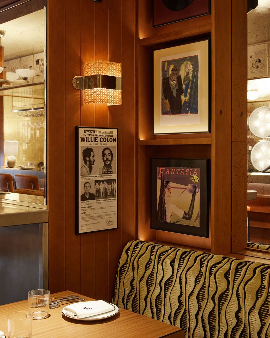 A stylish, close-up view of a dining booth with a vintage-retro aesthetic. A woven metal sconce with a warm glow illuminates a wall of wooden paneling and a vibrant banquette with a wavy, black and yellow pattern. The composition is a rich tapestry of textures, colors, and artful details. A stylish, close-up view of a dining booth with a vintage-retro aesthetic. A woven metal sconce with a warm glow illuminates a wall of wooden paneling and a vibrant banquette with a wavy, black and yellow pattern. The composition is a rich tapestry of textures, colors, and artful details.