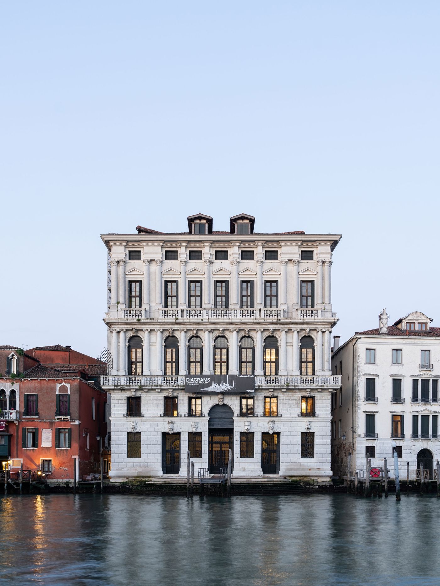 A grand, classical-style building with large windows and balconies overlooks a tranquil canal, surrounded by colorful Venetian architecture. A grand, classical-style building with large windows and balconies overlooks a tranquil canal, surrounded by colorful Venetian architecture.