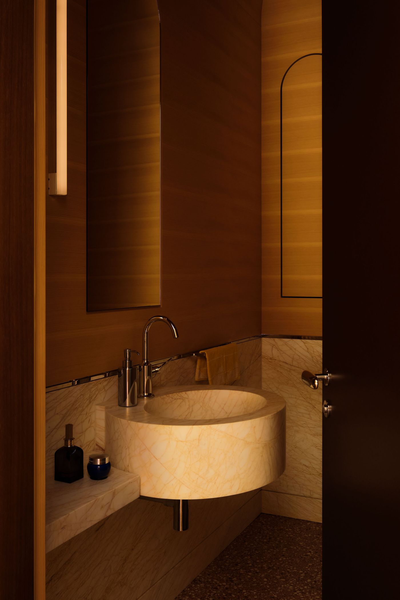 A modern, warmly lit bathroom featuring a marble sink, sleek fixtures, and wooden accents, creating a cozy yet elegant ambiance.