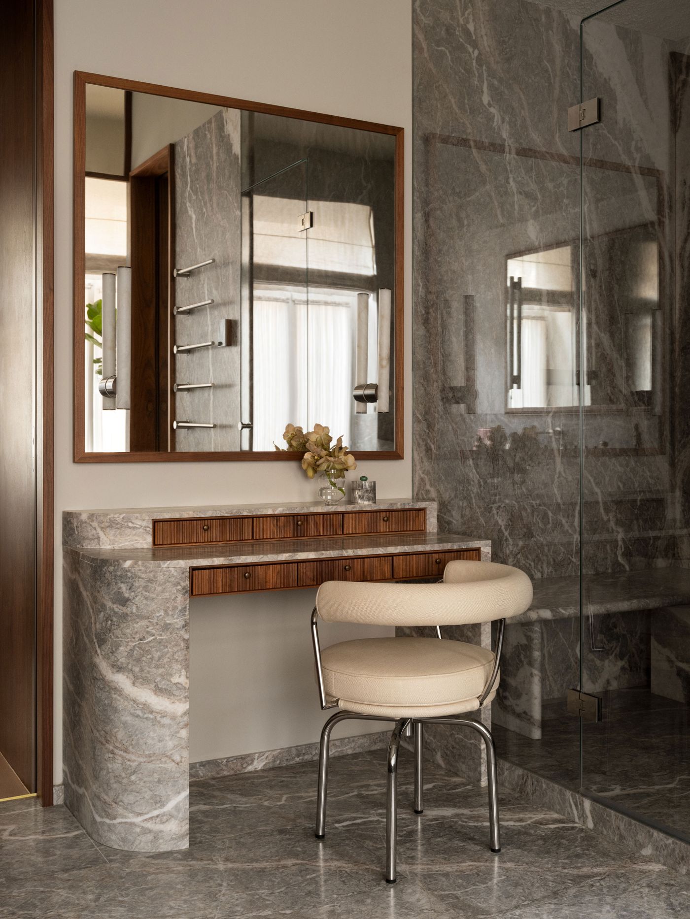 Modern bathroom vanity with a wooden mirror frame, marble countertop, and beige cushioned chair, surrounded by elegant marble walls. Modern bathroom vanity with a wooden mirror frame, marble countertop, and beige cushioned chair, surrounded by elegant marble walls.