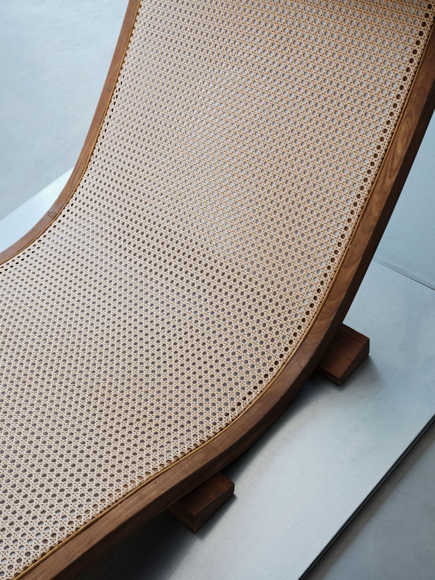 Detail of a chaise reveals the fine woven cane stretched across its gently curving timber frame. The tactile natural materials contrast with the cool, smooth metal platform beneath, encapsulating the project’s broader juxtaposition of warm, crafted elements with an industrial material palette. Detail of a chaise reveals the fine woven cane stretched across its gently curving timber frame. The tactile natural materials contrast with the cool, smooth metal platform beneath, encapsulating the project’s broader juxtaposition of warm, crafted elements with an industrial material palette.