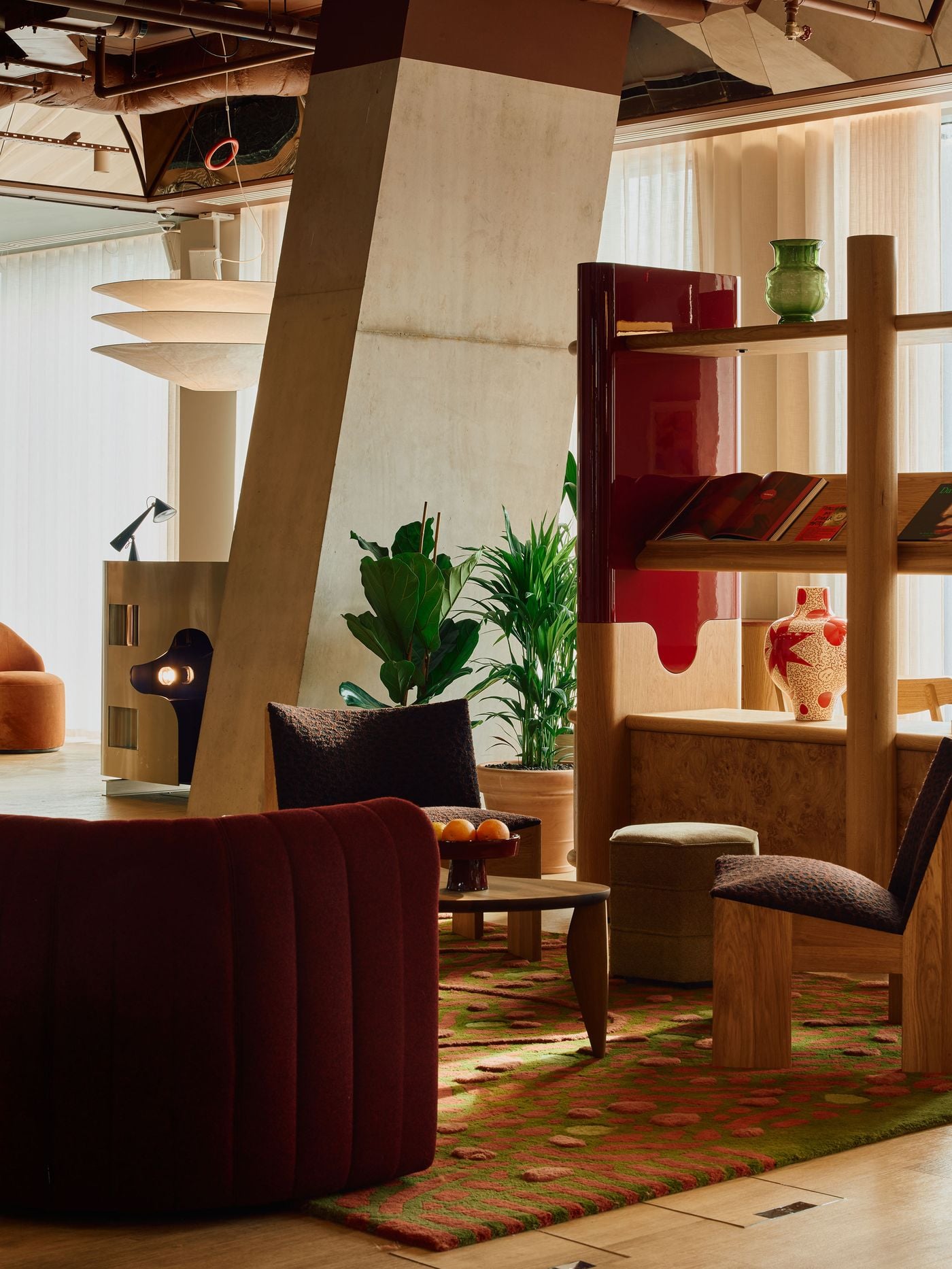 A richly layered lounge vignette brings together burgundy upholstery, patterned rugs, sculptural timber furniture and Holloway Li’s glossy red-lacquer joinery. The angular concrete column and exposed ceiling temper the retro warmth with a raw architectural edge, while the stainless-steel DJ booth glows in the background like a cinematic prop. A richly layered lounge vignette brings together burgundy upholstery, patterned rugs, sculptural timber furniture and Holloway Li’s glossy red-lacquer joinery. The angular concrete column and exposed ceiling temper the retro warmth with a raw architectural edge, while the stainless-steel DJ booth glows in the background like a cinematic prop.