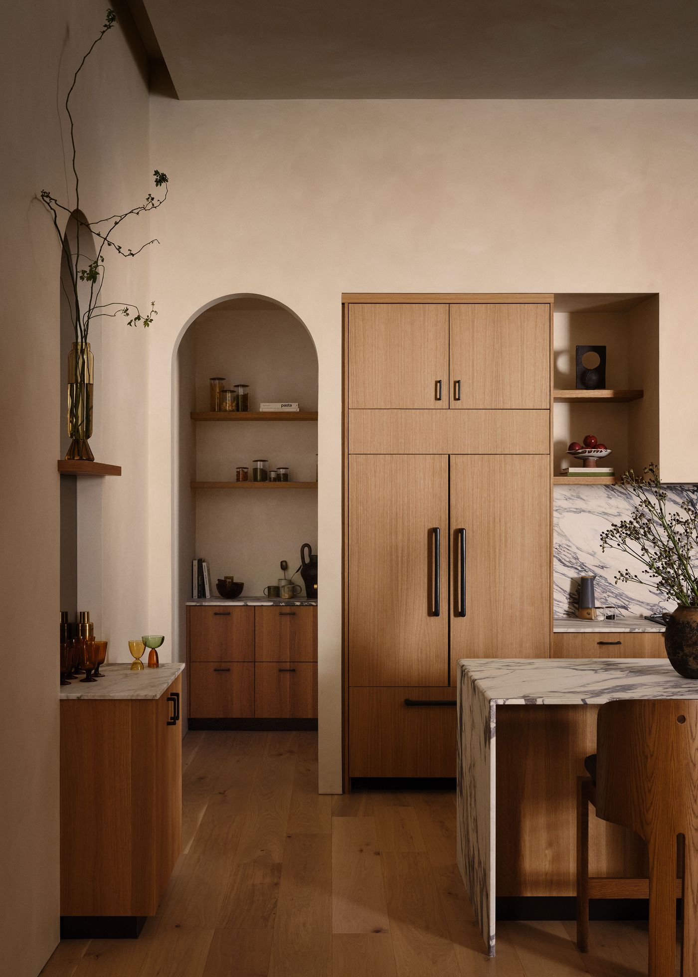 A modern kitchen with wooden cabinets, marble countertop, and a decorative vase, showcasing a warm and inviting aesthetic.