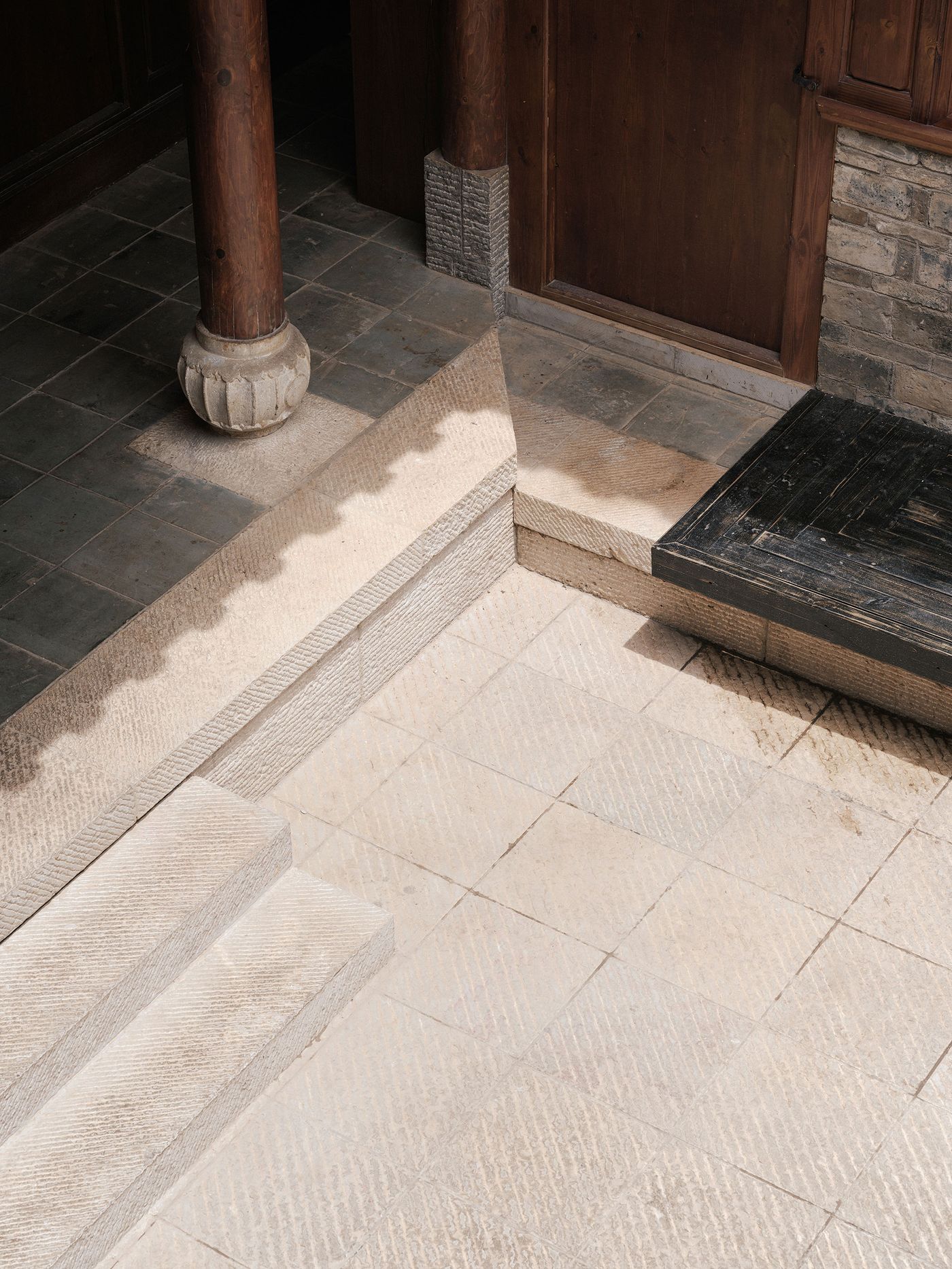 An angled view of a textured stone entrance with wooden doors and a supporting column, featuring steps and a wooden platform. An angled view of a textured stone entrance with wooden doors and a supporting column, featuring steps and a wooden platform.