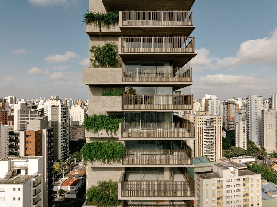 A mid-level aerial view of the tower, revealing its distinctive staggered concrete balconies adorned with lush, cascading greenery. The building's biophilic design seamlessly integrates natural elements into its brutalist framework, offering a refreshing contrast against the dense urban backdrop.