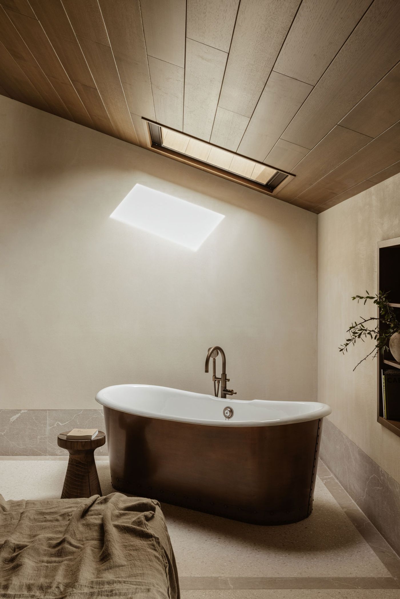 A captivating open-plan bathroom space features a dramatic freestanding copper bathtub, positioned beneath a luminous rectangular skylight that bathes the room in natural light. The sloped timber ceiling adds warmth and texture, contrasting with the smooth, earthy-toned walls and floor, creating a luxurious and immersive experience. A captivating open-plan bathroom space features a dramatic freestanding copper bathtub, positioned beneath a luminous rectangular skylight that bathes the room in natural light. The sloped timber ceiling adds warmth and texture, contrasting with the smooth, earthy-toned walls and floor, creating a luxurious and immersive experience.