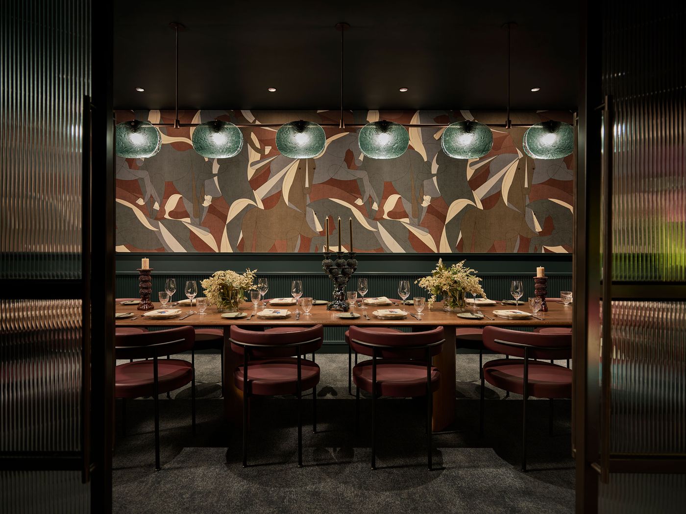 Elegant dining room featuring a large wooden table, stylish chairs, floral centerpieces, and artistic wallpaper, illuminated by glass pendant lights. Elegant dining room featuring a large wooden table, stylish chairs, floral centerpieces, and artistic wallpaper, illuminated by glass pendant lights.