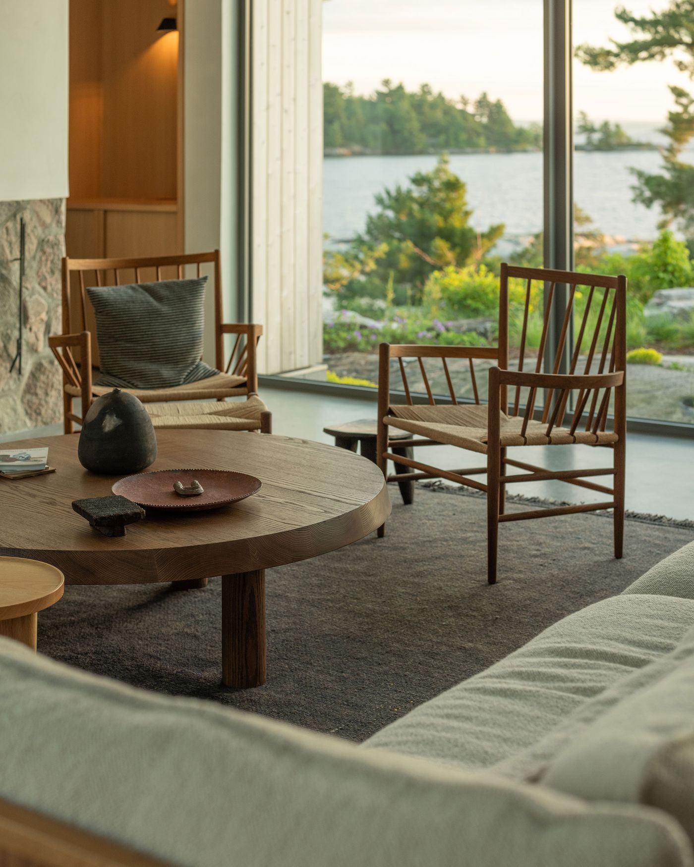 Cozy modern living room featuring wooden furniture, a round table, and large windows showcasing a serene waterfront view.
