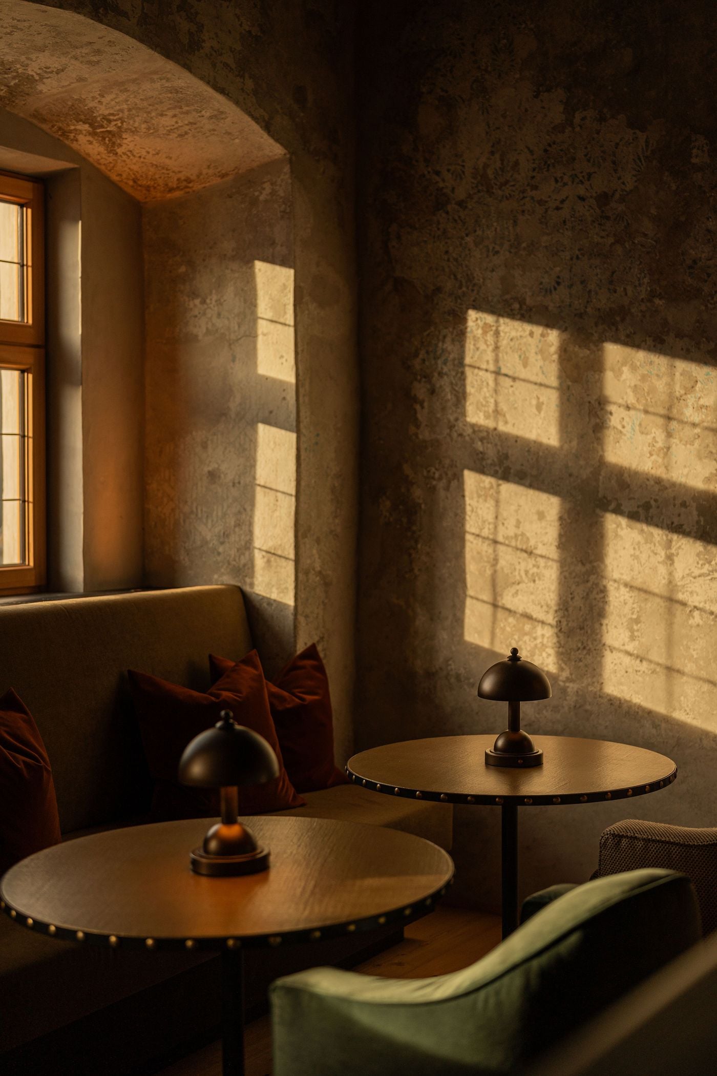 Sunlight projects the grid of a deep-set window onto a mottled, time-worn plaster wall in a corner of Castel Badia's bar lounge. Two round tables edged with brass studs hold small domed lamps, flanked by a banquette with russet velvet cushions and a moss-green velvet armchair. Sunlight projects the grid of a deep-set window onto a mottled, time-worn plaster wall in a corner of Castel Badia's bar lounge. Two round tables edged with brass studs hold small domed lamps, flanked by a banquette with russet velvet cushions and a moss-green velvet armchair.