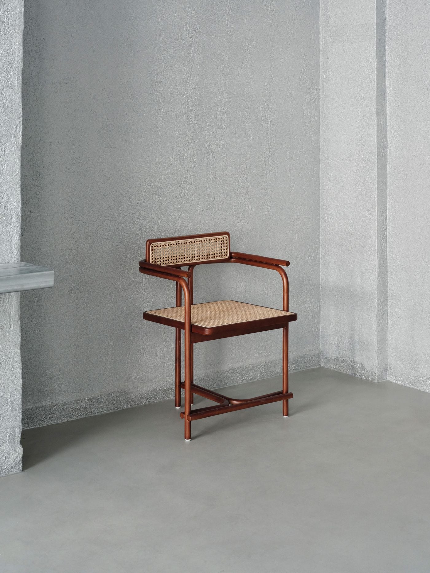A timber-and-cane chair stands almost as an object on display against the gallery’s textured silvery-grey walls. Its warm reddish timber and woven seat and backrest provide a restrained counterpoint to the cool monochromatic setting, while the sparse composition emphasises the chair’s elegant tubular geometry. A timber-and-cane chair stands almost as an object on display against the gallery’s textured silvery-grey walls. Its warm reddish timber and woven seat and backrest provide a restrained counterpoint to the cool monochromatic setting, while the sparse composition emphasises the chair’s elegant tubular geometry.