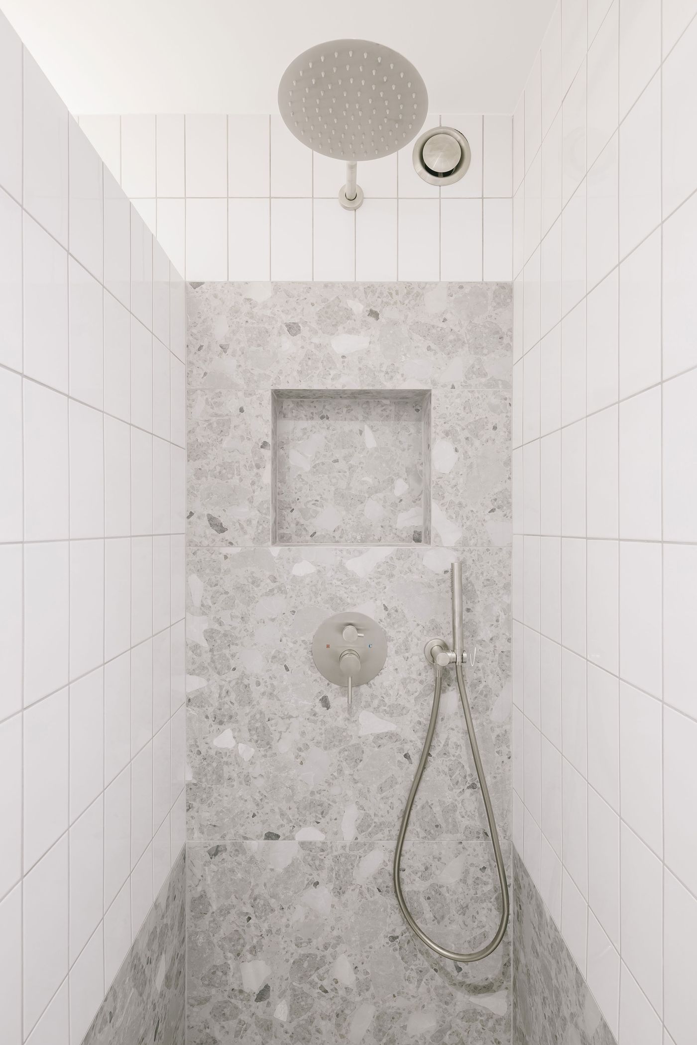 A modern shower with a round overhead showerhead, a sleek faucet, and textured gray stone walls, featuring a recessed nook.