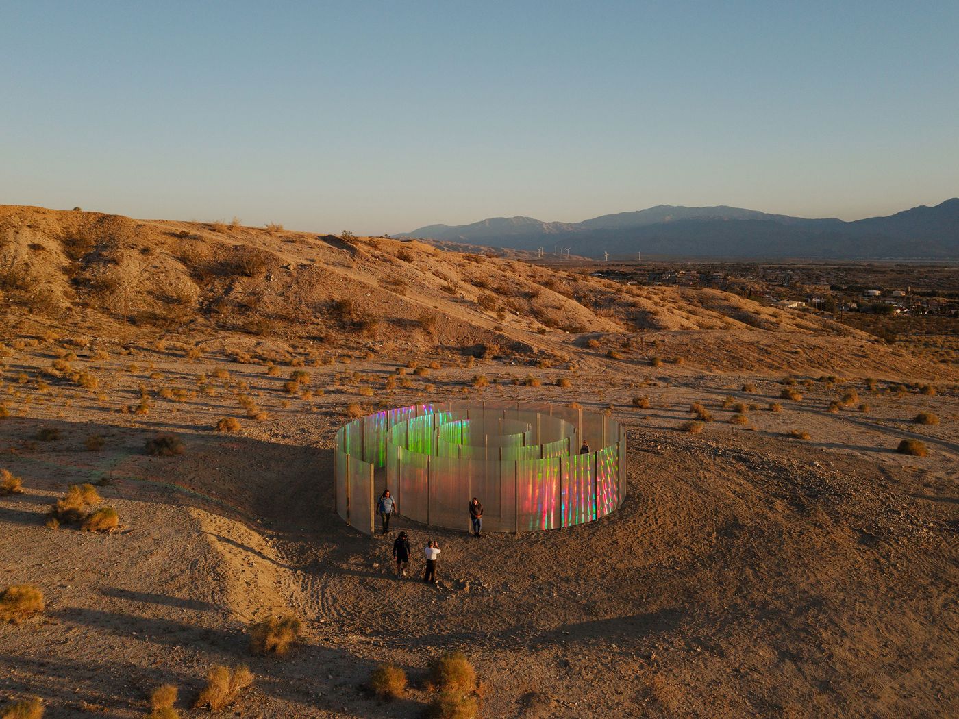 An iridescent spiral installation in a desert landscape, reflecting sunlight amidst a backdrop of suburban homes. An iridescent spiral installation in a desert landscape, reflecting sunlight amidst a backdrop of suburban homes.