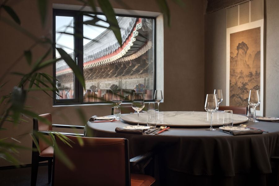 A beautifully set dining table with glasses, plates, and chopsticks, framed by a window showcasing traditional architecture outside.