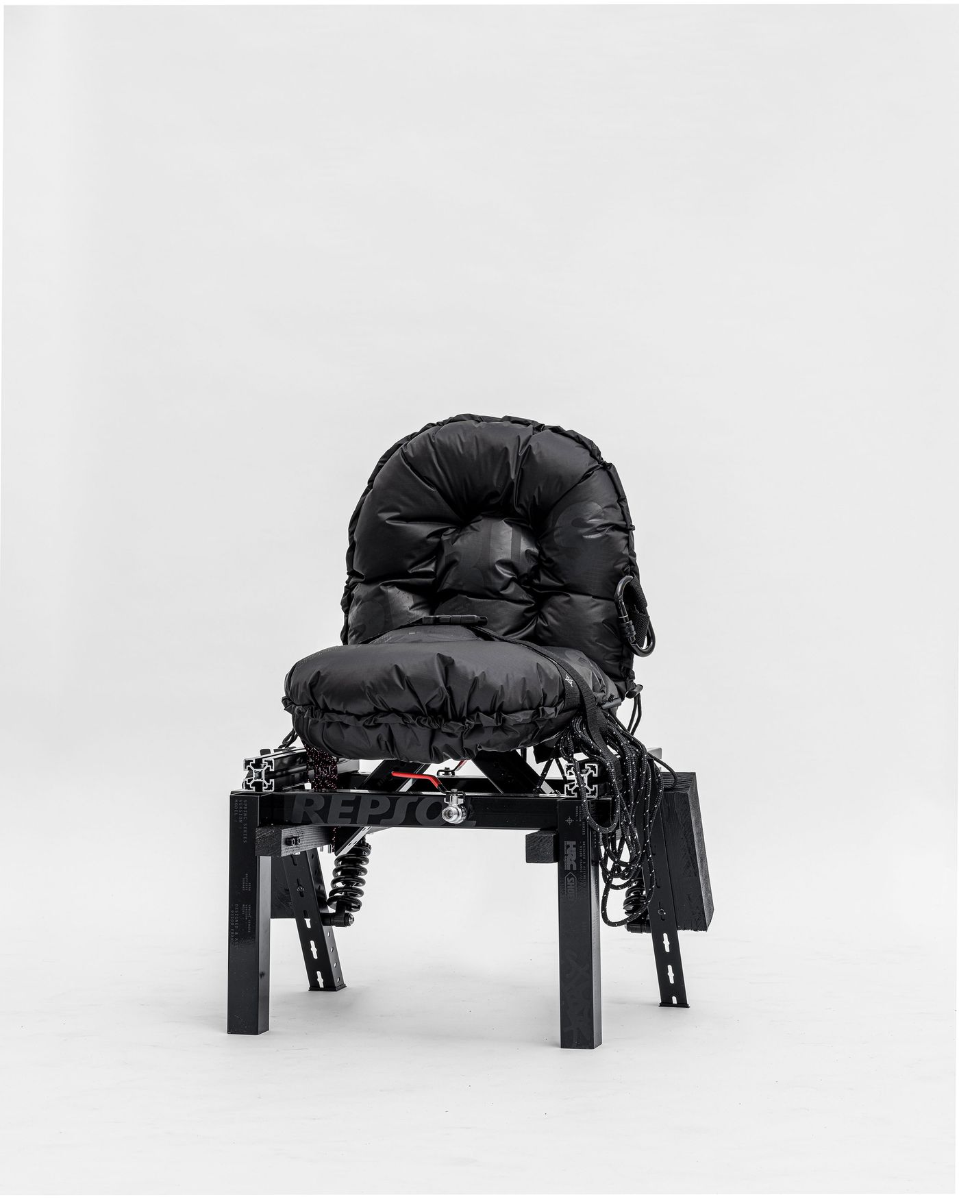 A black, padded chair with a structured base and various cables, set against a plain light backdrop. A black, padded chair with a structured base and various cables, set against a plain light backdrop.