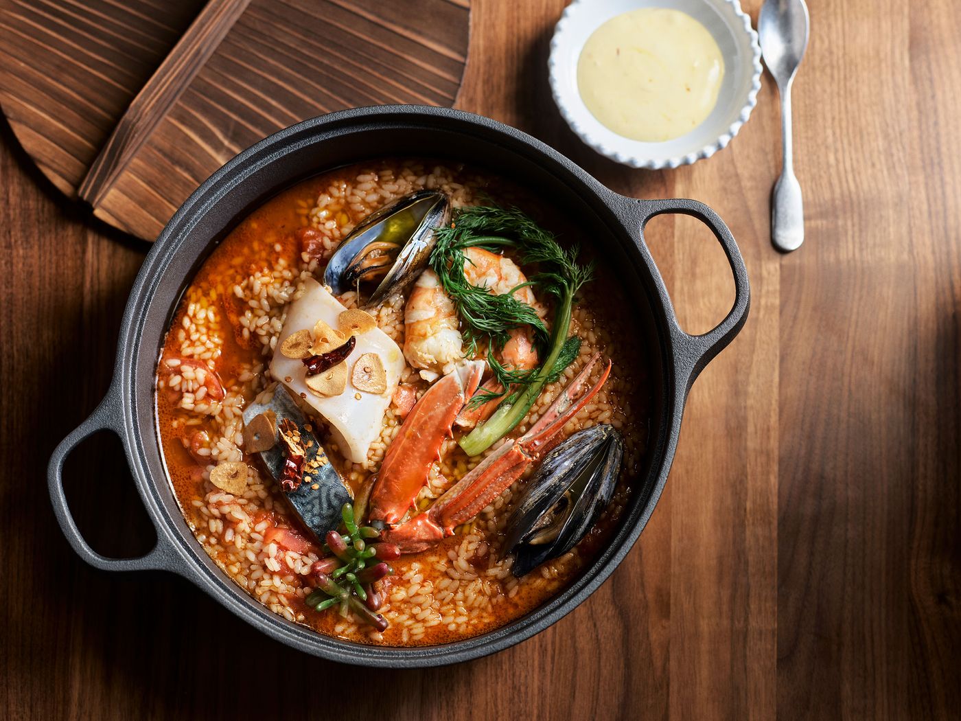 A flavorful seafood paella in a black pot, featuring shrimp, crab, and mussels, garnished with herbs and spices, paired with a creamy sauce. A flavorful seafood paella in a black pot, featuring shrimp, crab, and mussels, garnished with herbs and spices, paired with a creamy sauce.